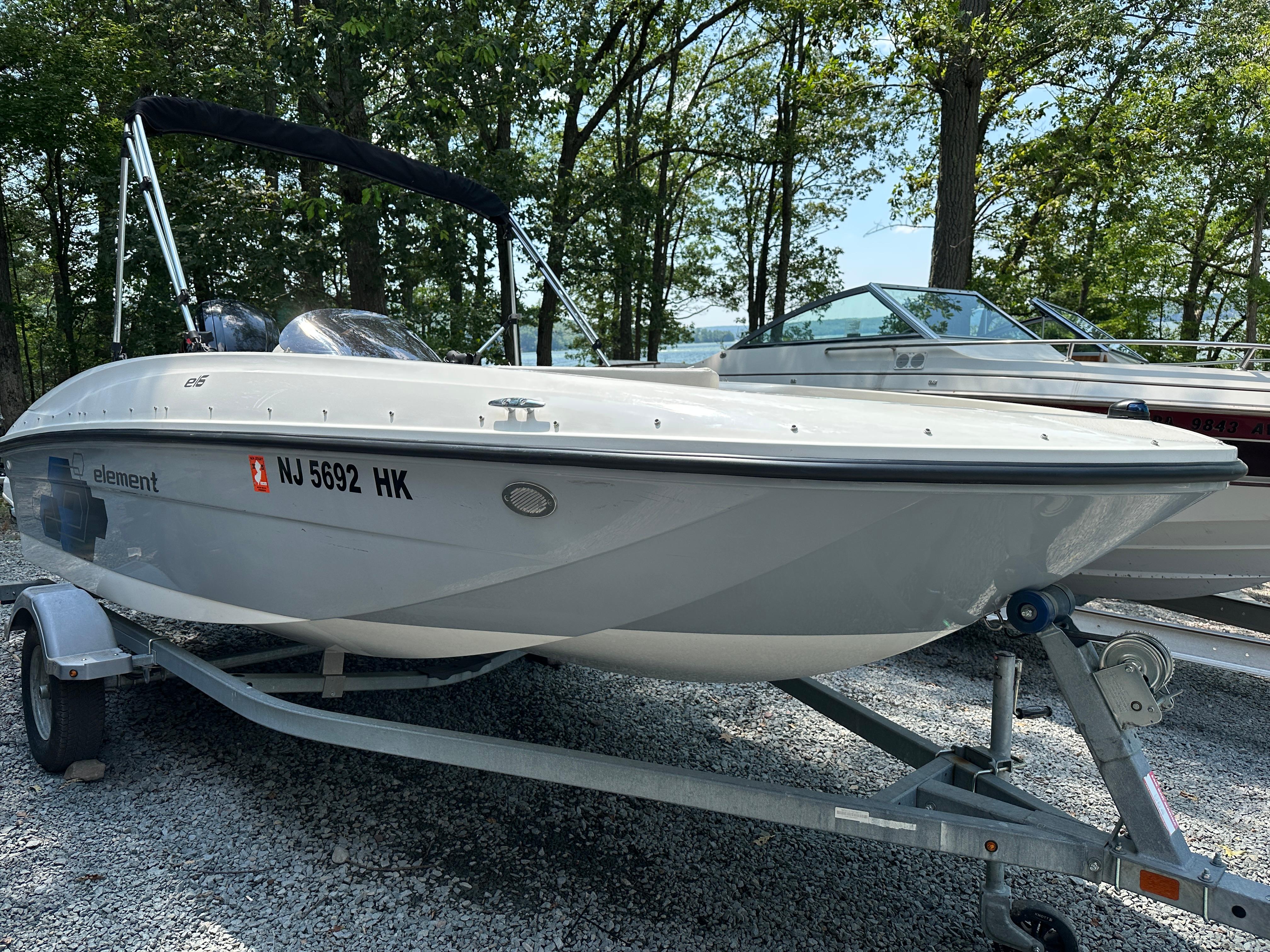 2019 Bayliner Element E16 boat on trailer, parked on gravel, surrounded by trees.