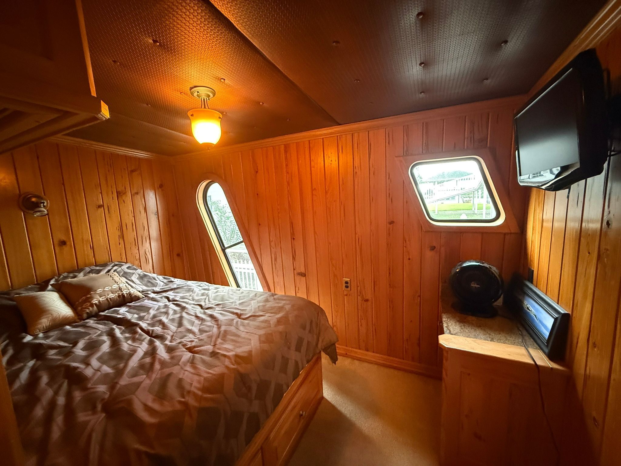 Cozy bedroom with wooden walls, a bed, a small TV, and a window overlooking outside.