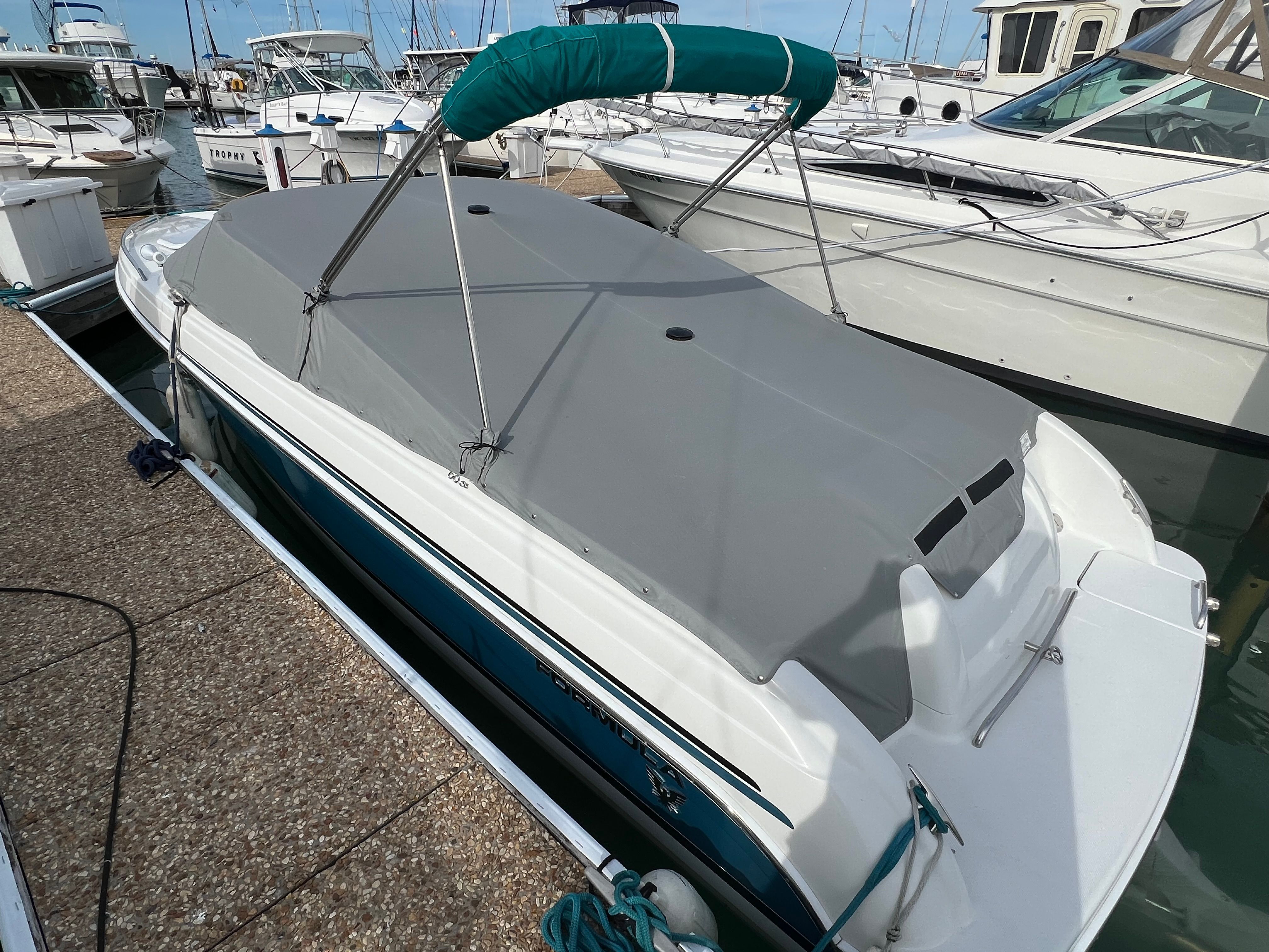 A 2005 Formula 260 Sun Sport with a gray cover is docked, surrounded by other boats.