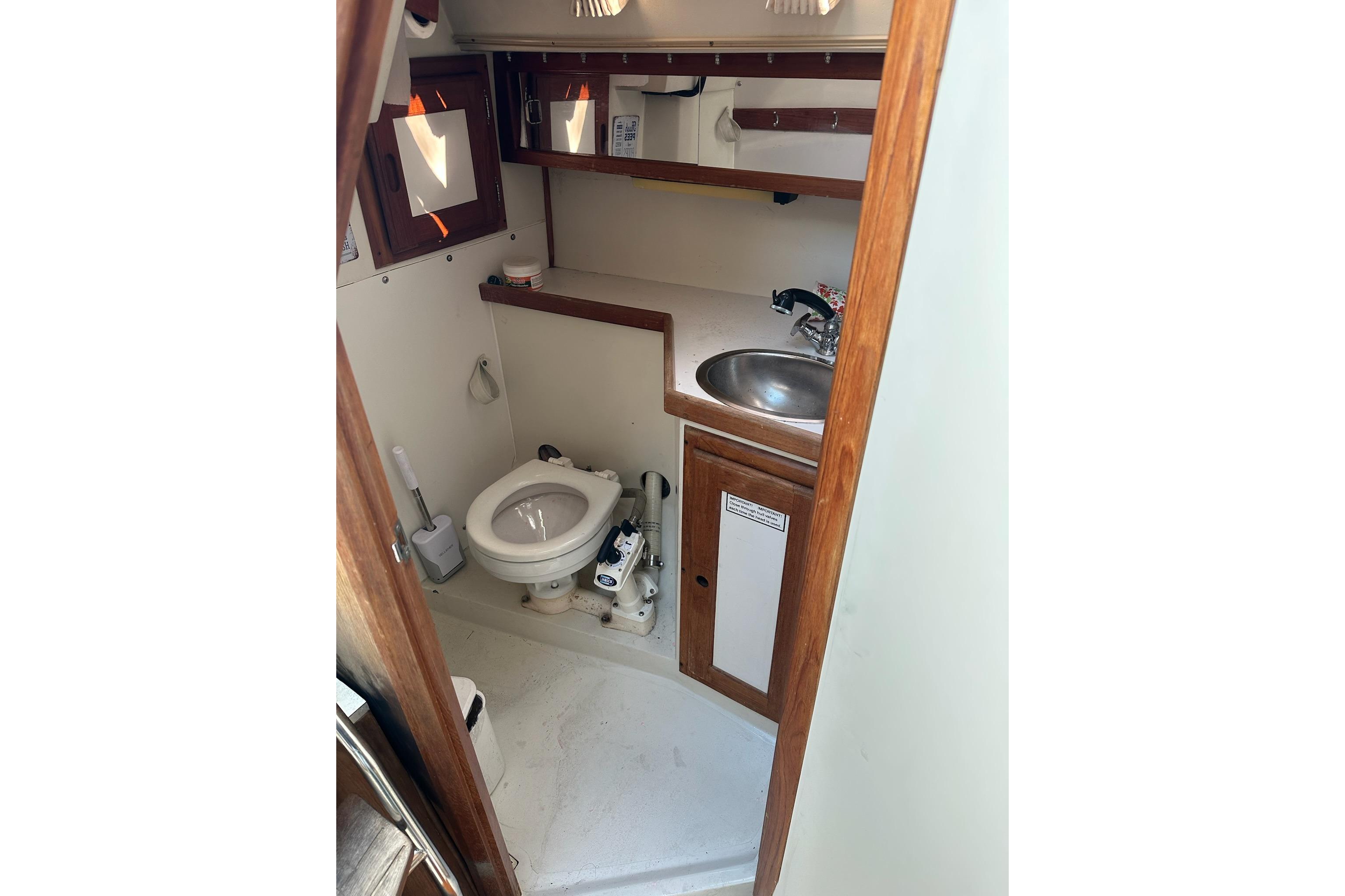 1991 Catalina 28 sailboat bathroom with toilet, sink, and wooden cabinetry.