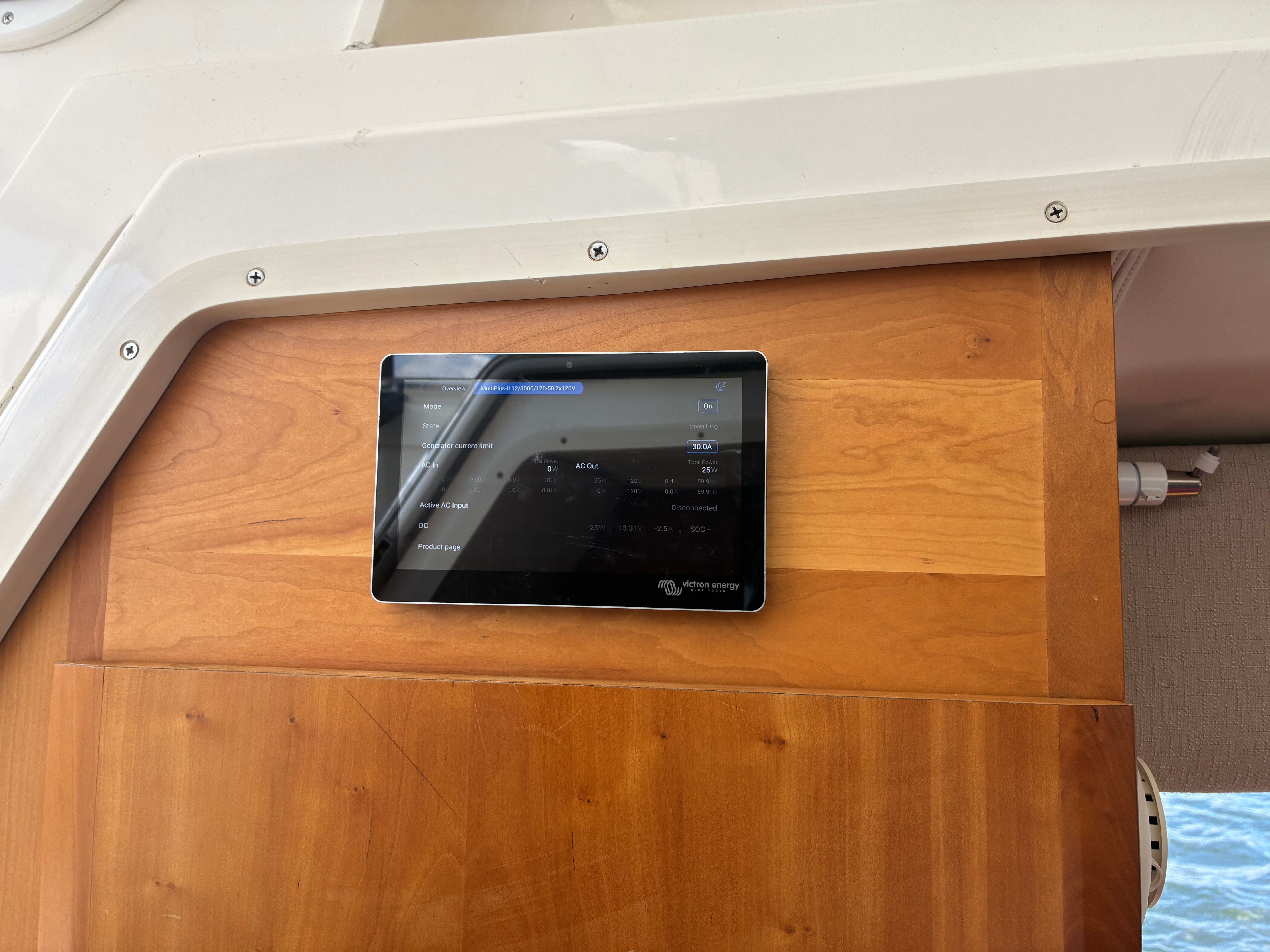 A modern control tablet is mounted on a wooden wall inside a yacht.