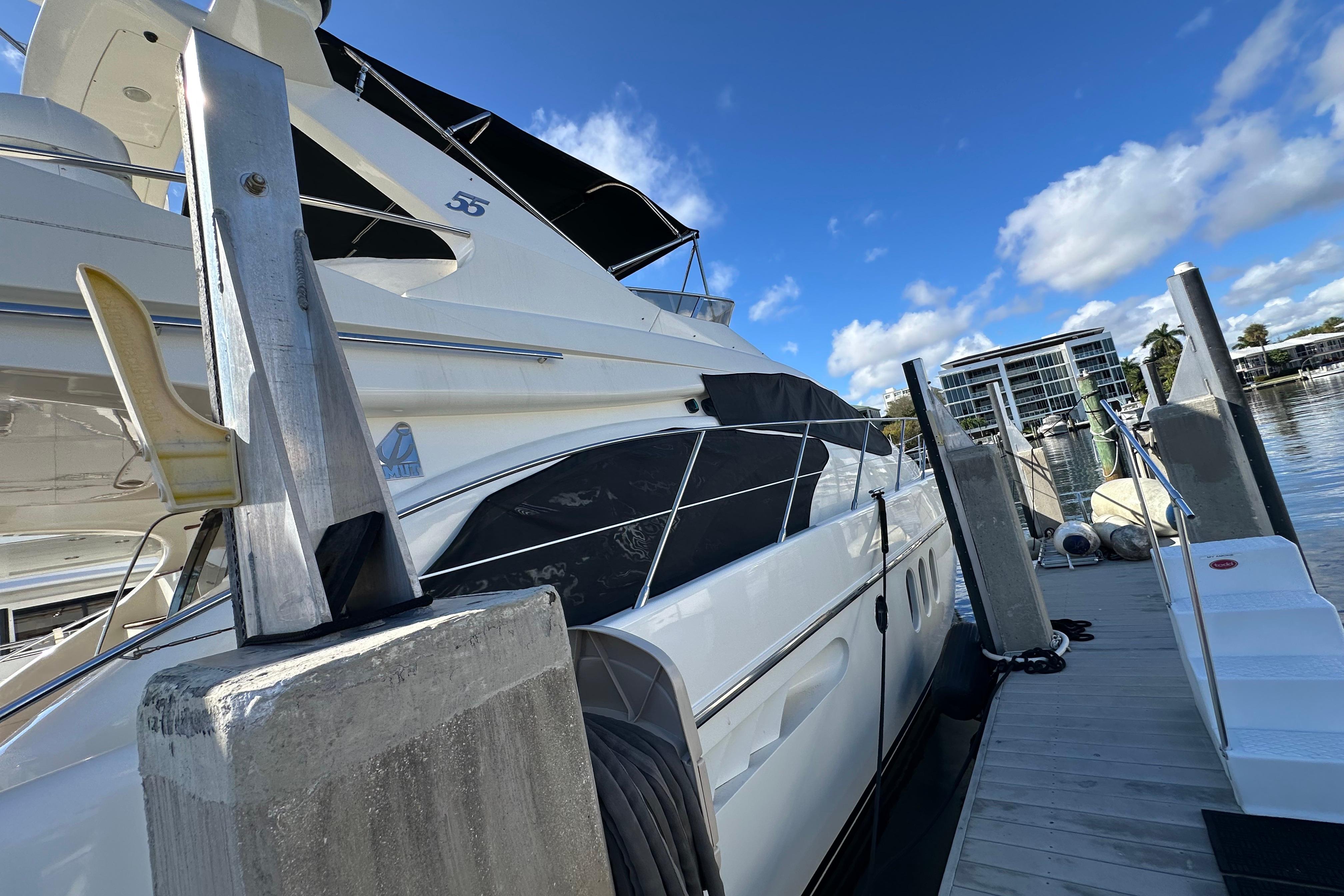 Azimut 55E 2004 yacht docked at marina, clear sky, modern waterfront buildings.