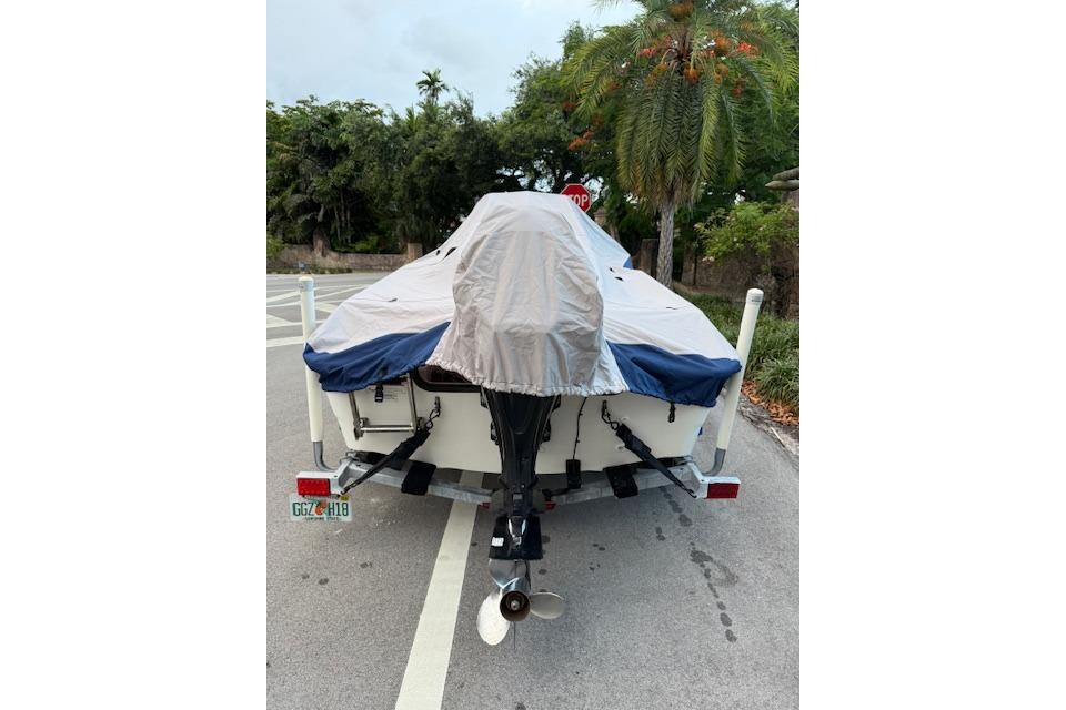 Covered 2016 Boston Whaler 150 Montauk boat on trailer, parked near tropical trees.