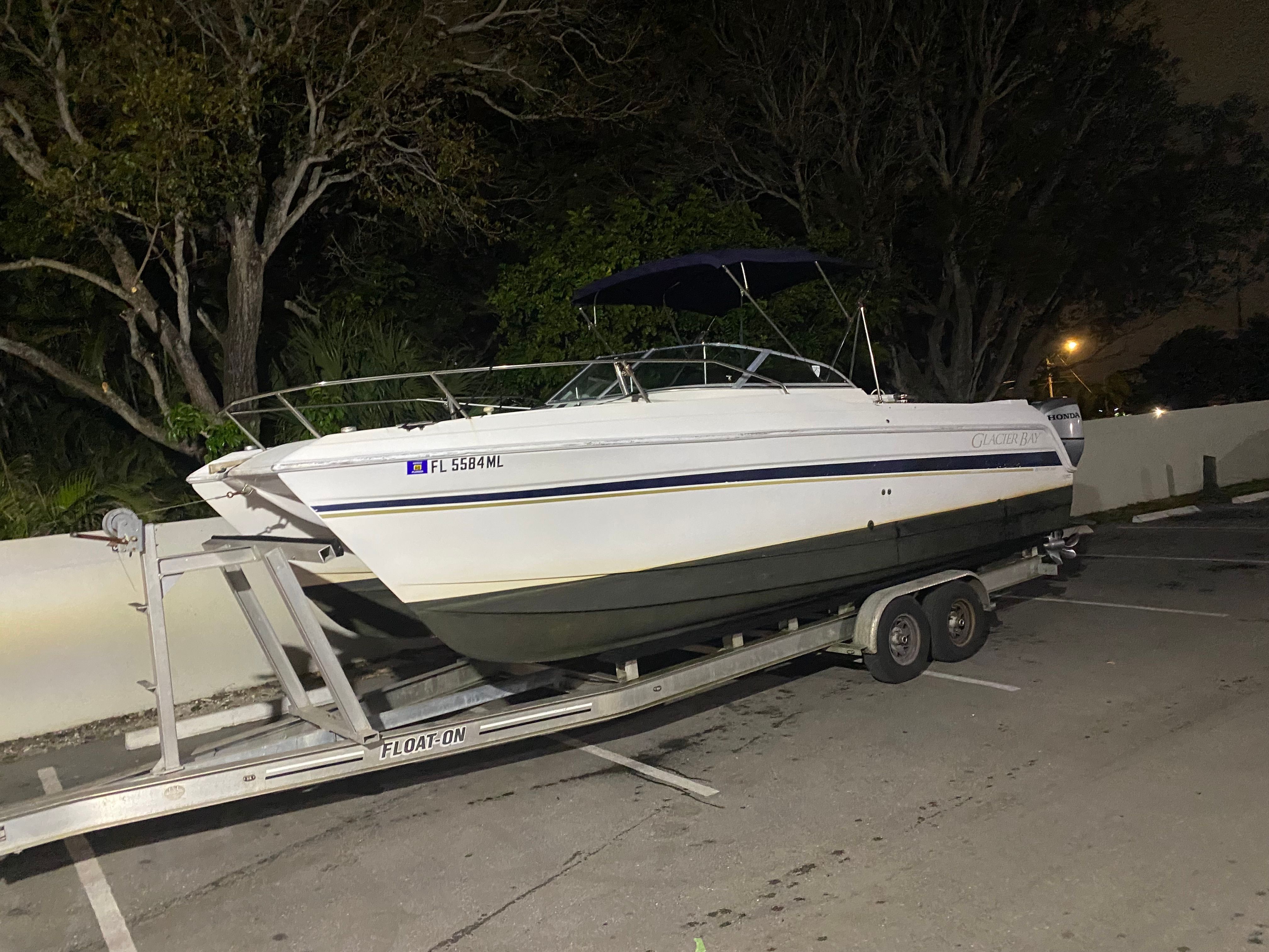 A 2003 Glacier Bay RENEGADE boat on a trailer in a parking lot.