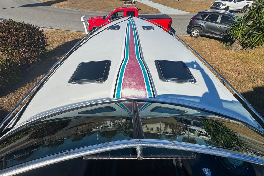 1989 Formula 292 SR-1 boat with colorful stripes, parked near a red truck and gray car.