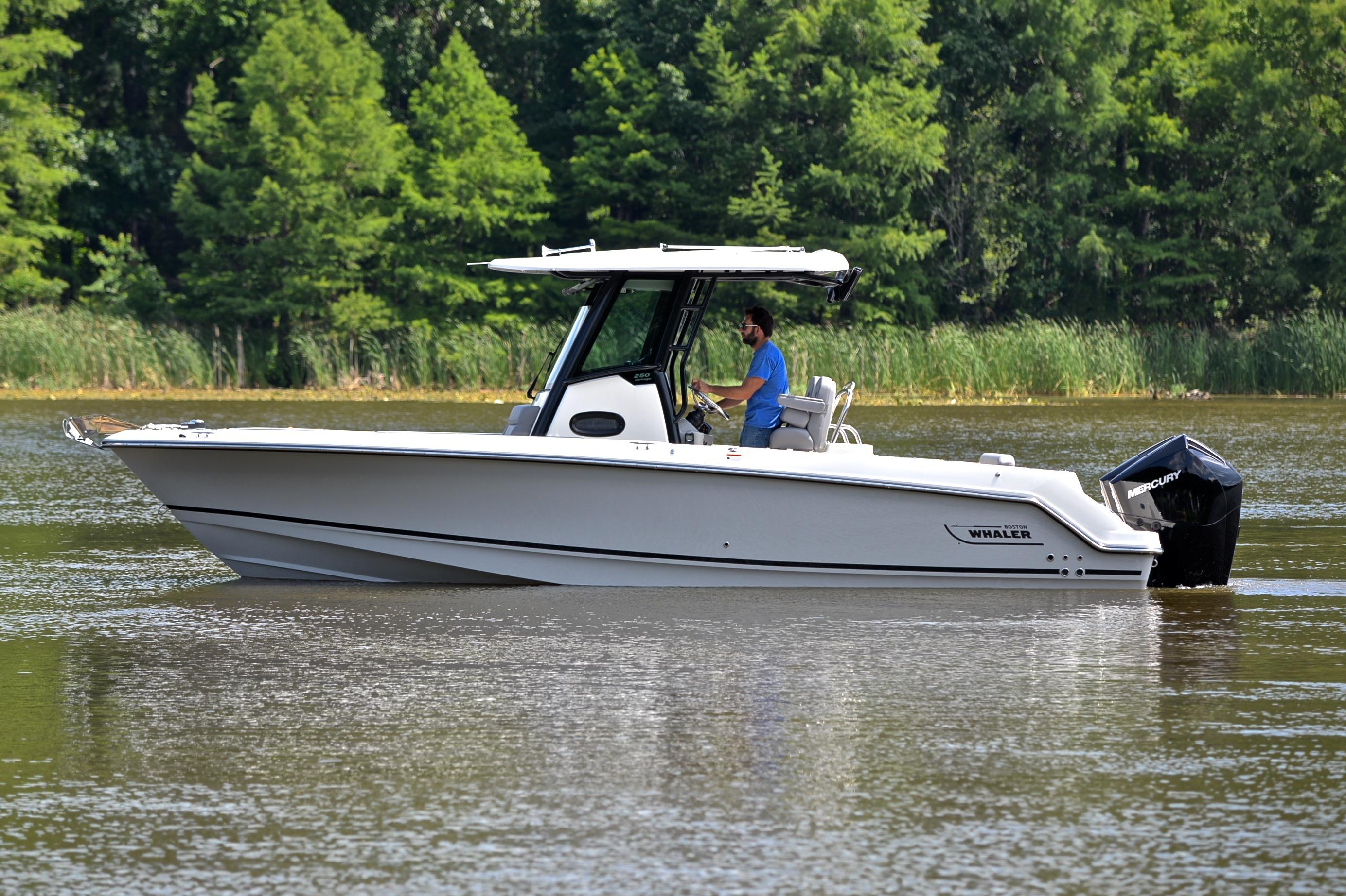 2024 Boston Whaler 250 Outrage boat cruising on a calm lake with lush greenery.