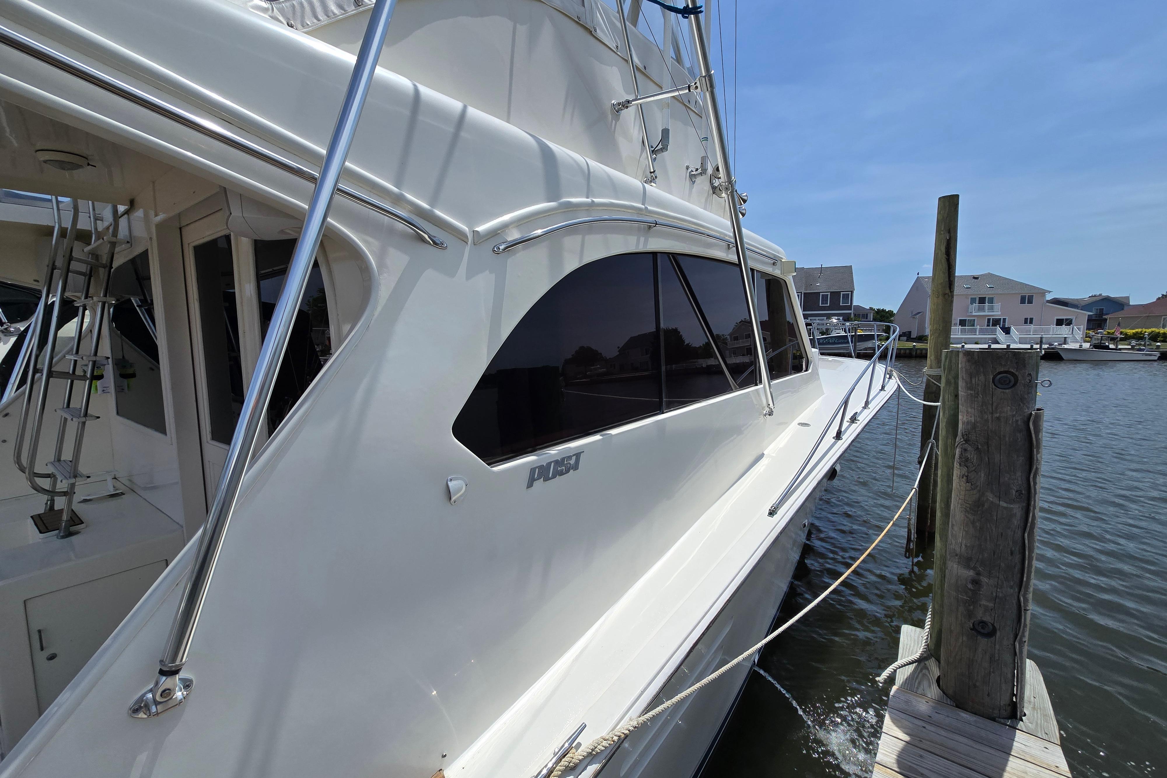 1988 Post 46 Convertible yacht docked by waterfront homes under clear blue sky.