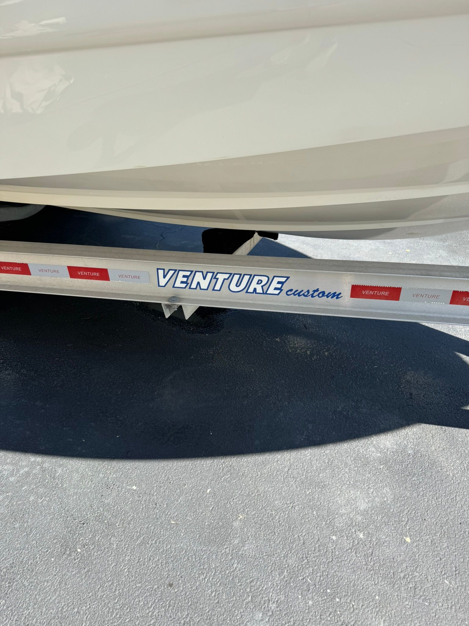 A boat trailer with "Venture Custom" written on it, parked on a lot.
