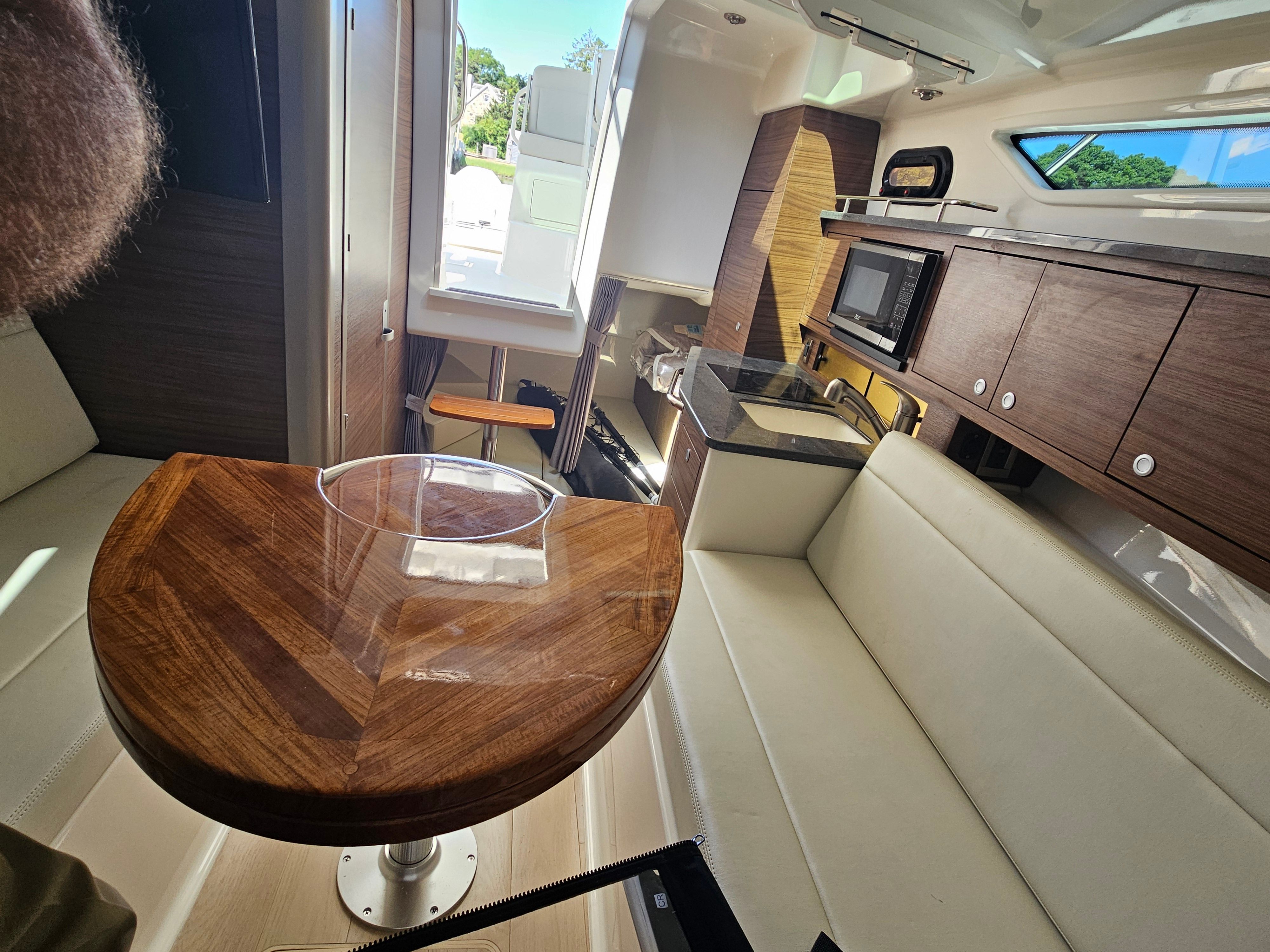 Interior of the Boston Whaler 325 Conquest with wooden table, white sofa, and kitchenette.