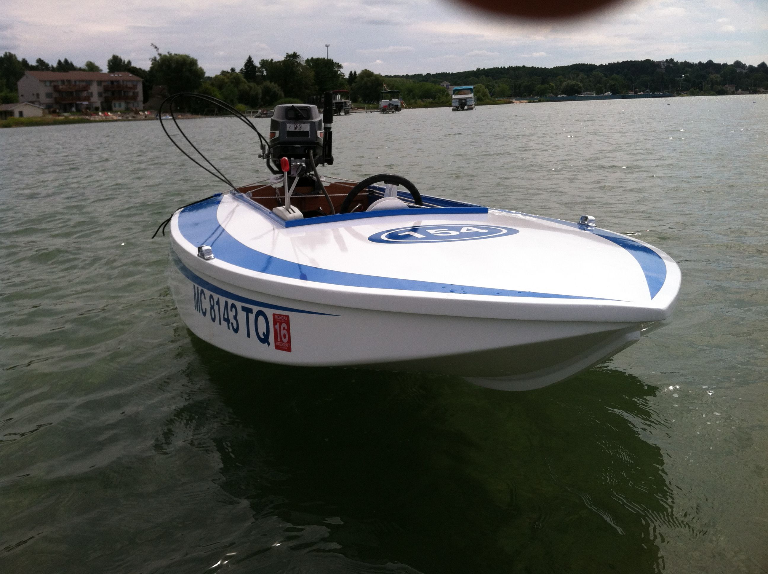 A small white racing boat with blue stripes on a calm lake.