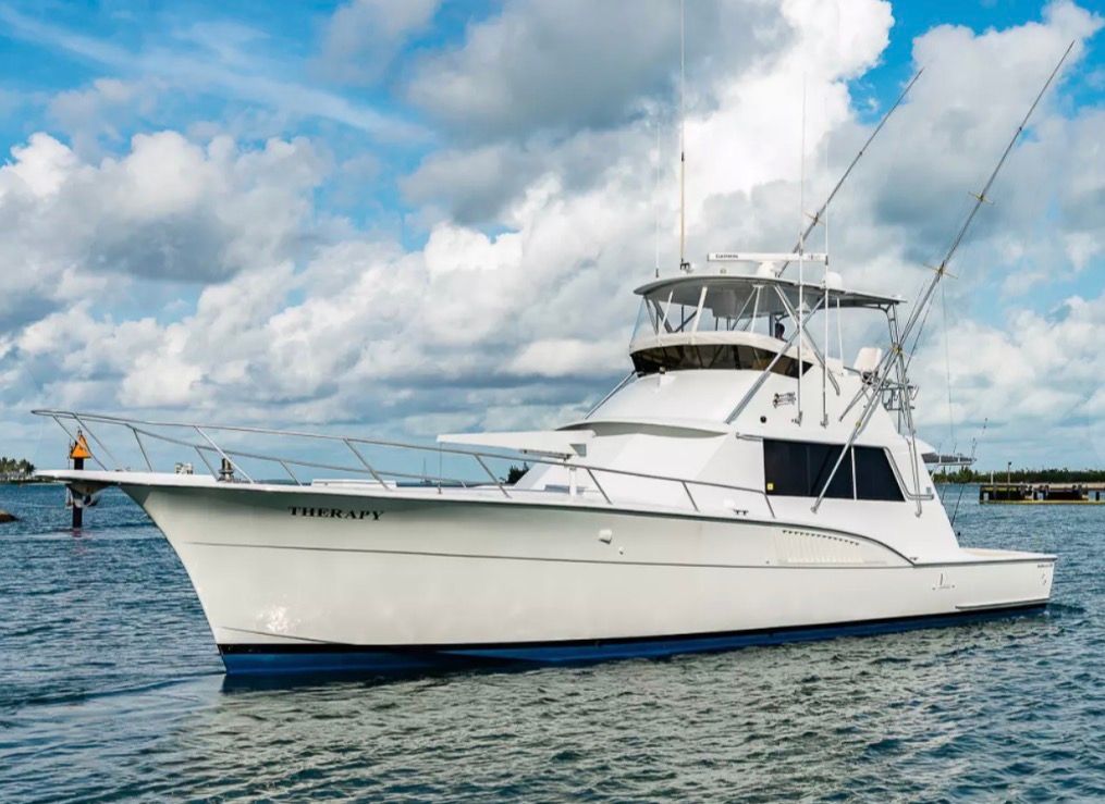 A 1979 Hatteras sport fishing boat on the water with blue sky and clouds.