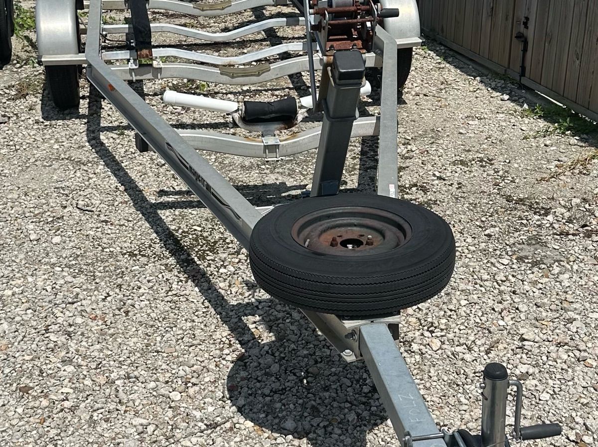A boat trailer on a gravel lot, without a boat on it.