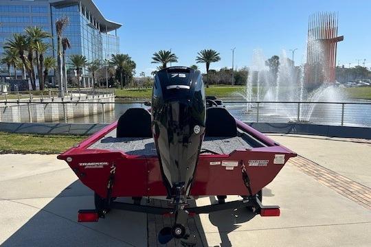 2026 Tracker Pro Team 175 boat, red, parked near a fountain and modern building.