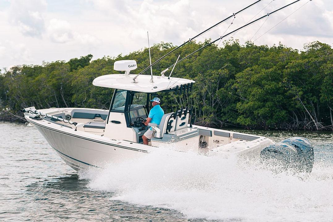 Manufacturer Provided Image: 2025 Cobia 285 Open Center Console boat cruising on water near lush greenery.
