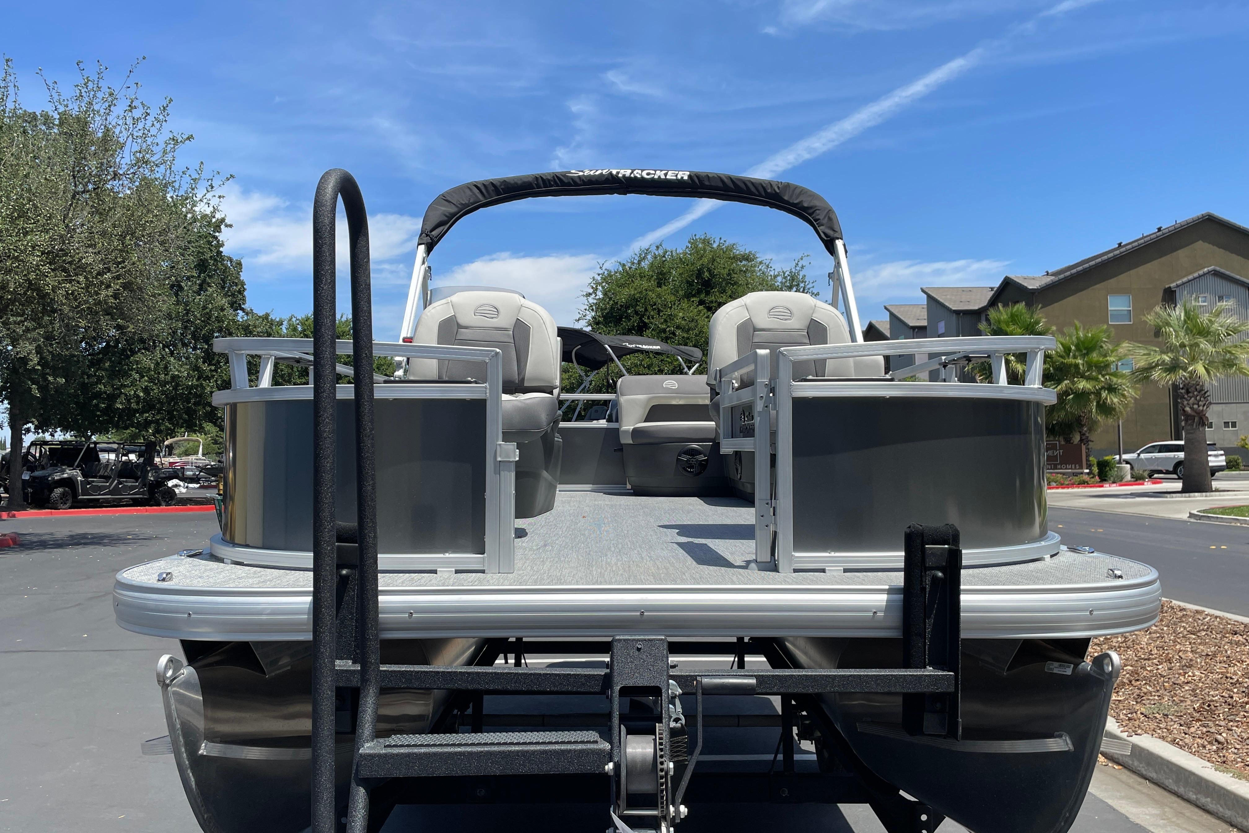 2026 Sun Tracker Bass Buggy 16 XL Select pontoon boat on trailer, parked outdoors.