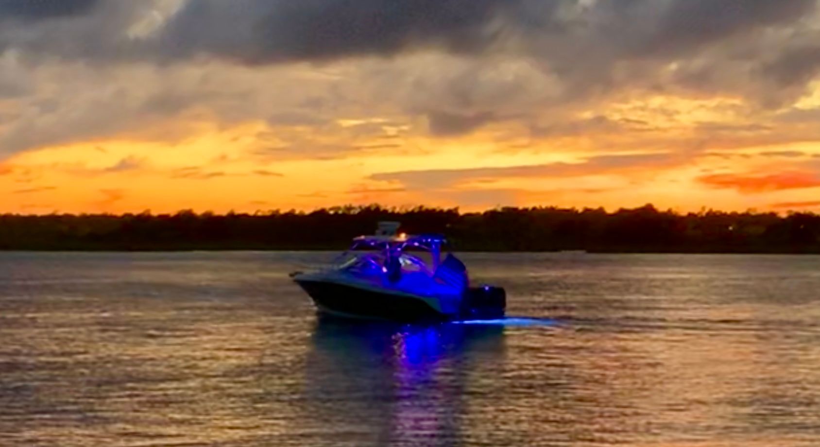 A Hydra-Sports Vector-VX boat on the water at sunset with blue lighting.