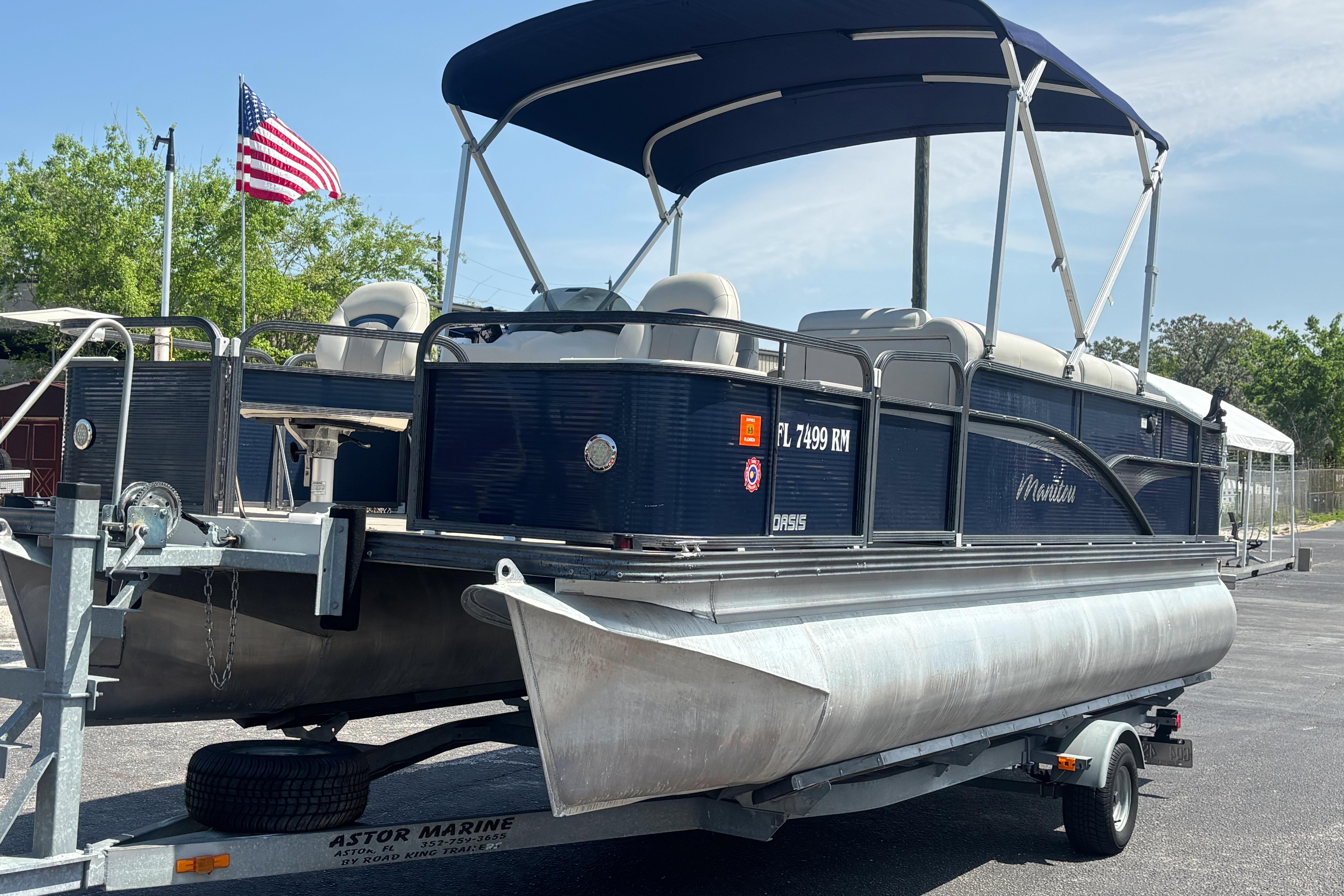 2015 Manitou 20 Oasis Angler pontoon boat on trailer with American flag in background.