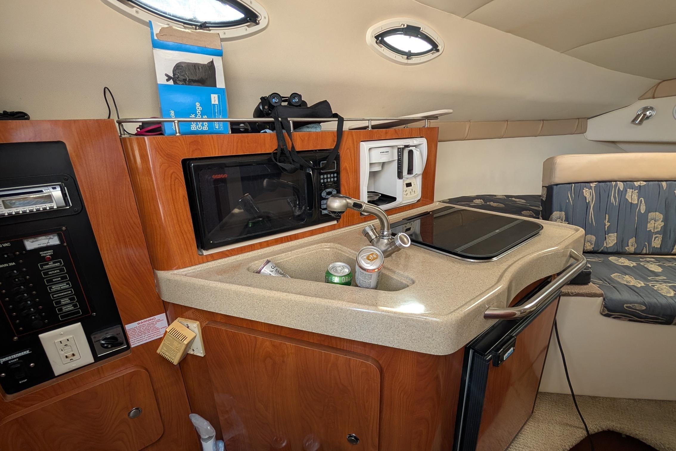 2004 Larson Cabrio 260 cabin interior with kitchenette, featuring sink, microwave, and seating area.