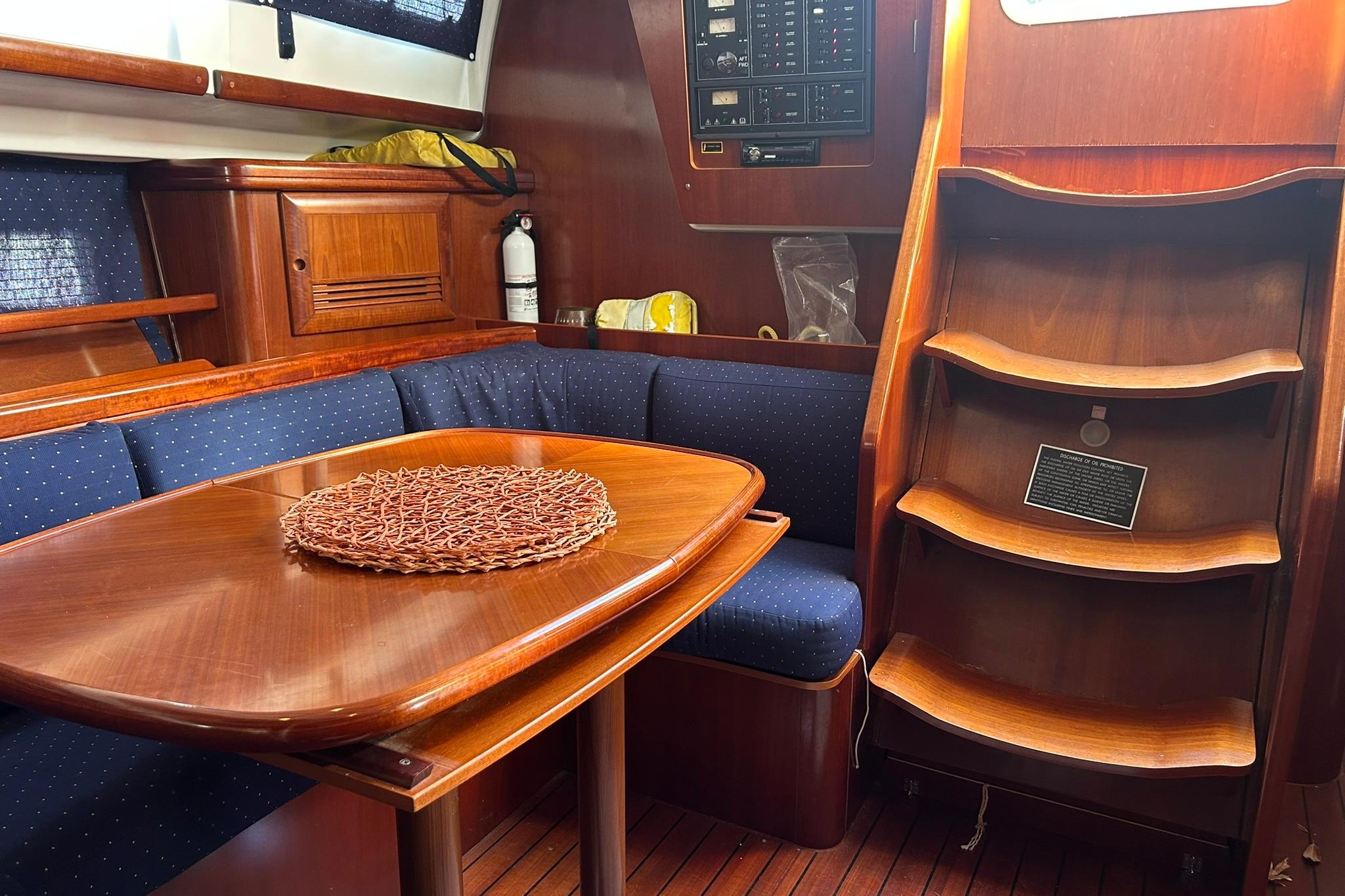 Interior of 2003 Beneteau Oceanis 42CC yacht with wooden table and blue seating.