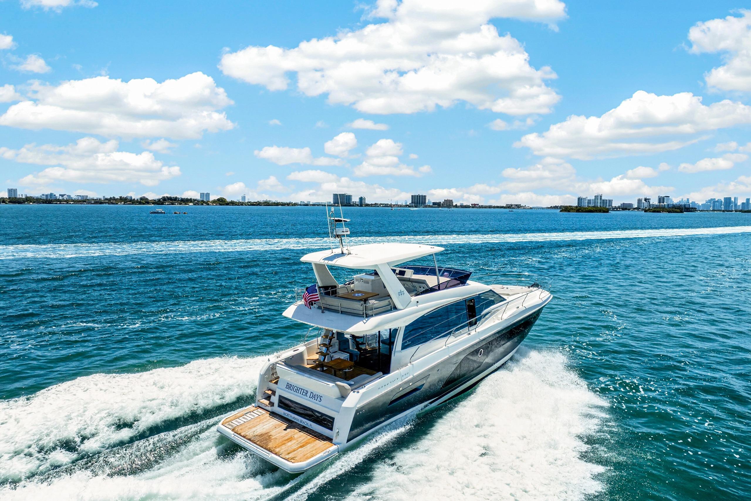 Luxurious 2023 Prestige 590 yacht cruising on a sunny day with city skyline backdrop.