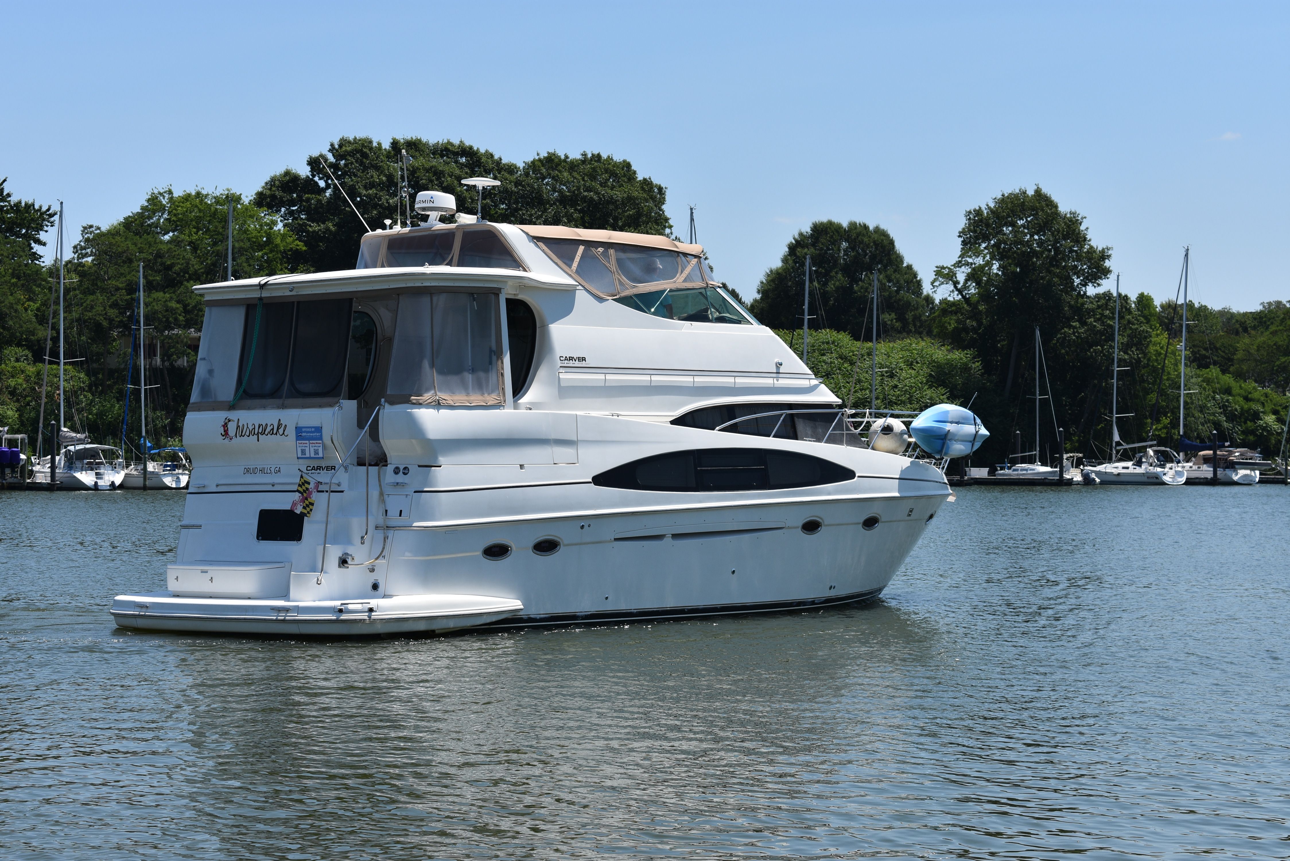 A white motor yacht sits calmly on the water, surrounded by trees and other boats.