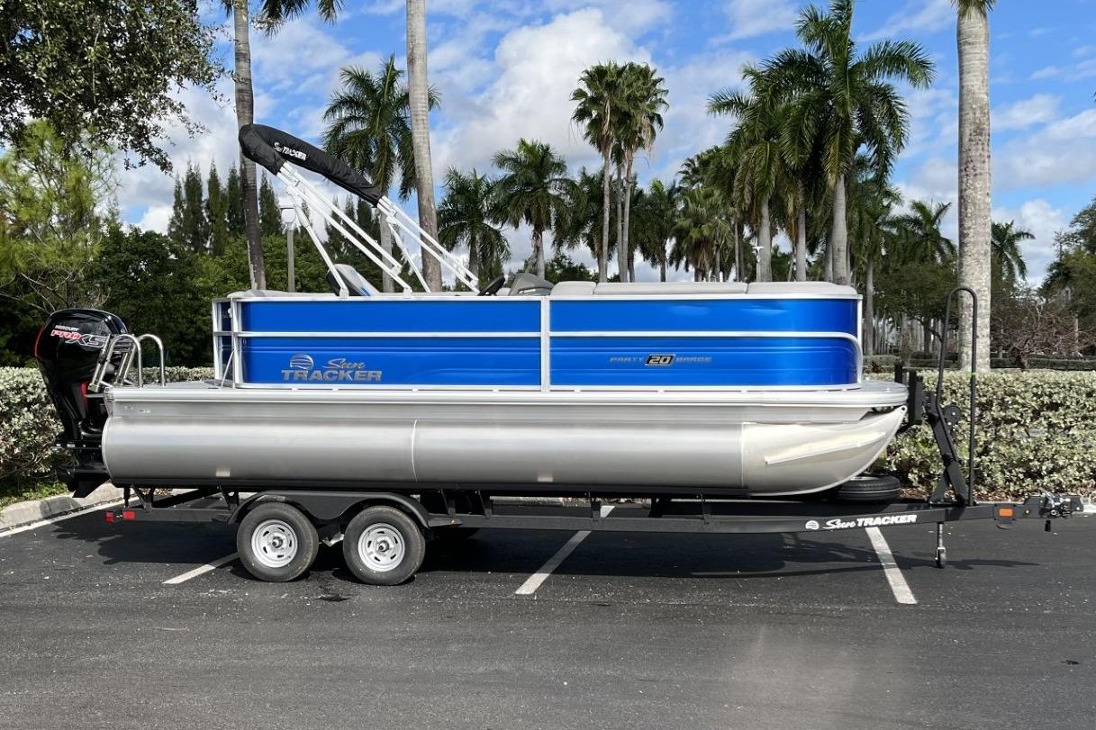 2026 Sun Tracker Party Barge 20 DLX pontoon boat on trailer, parked with palm trees.