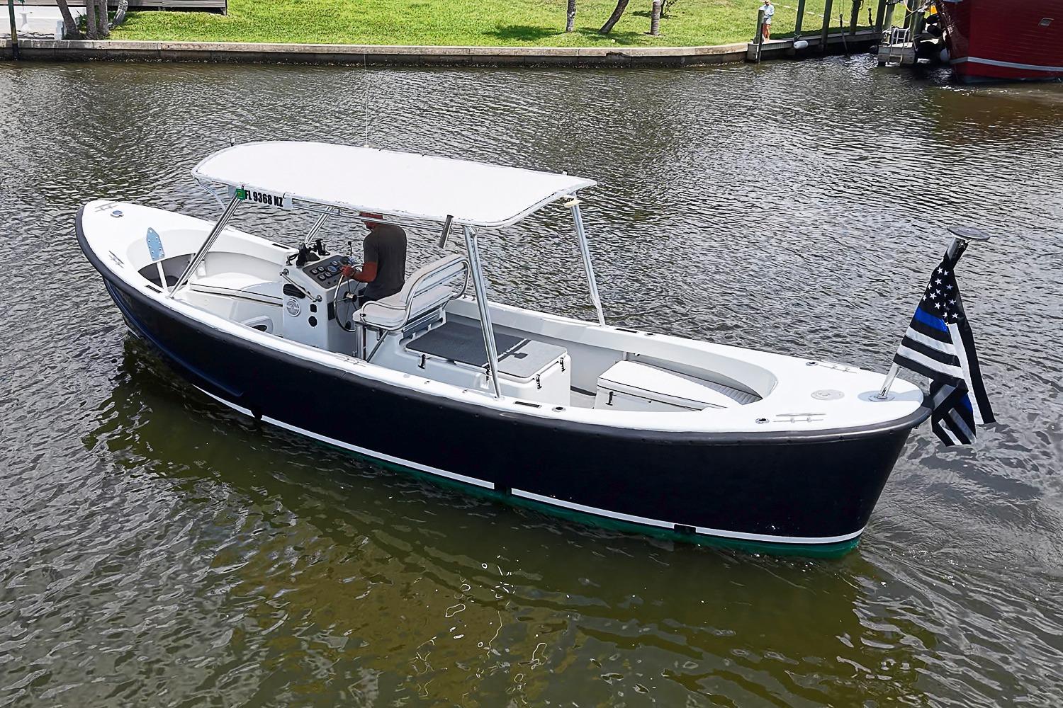 Custom 1969 boat with canopy and flag, cruising on a calm waterway.