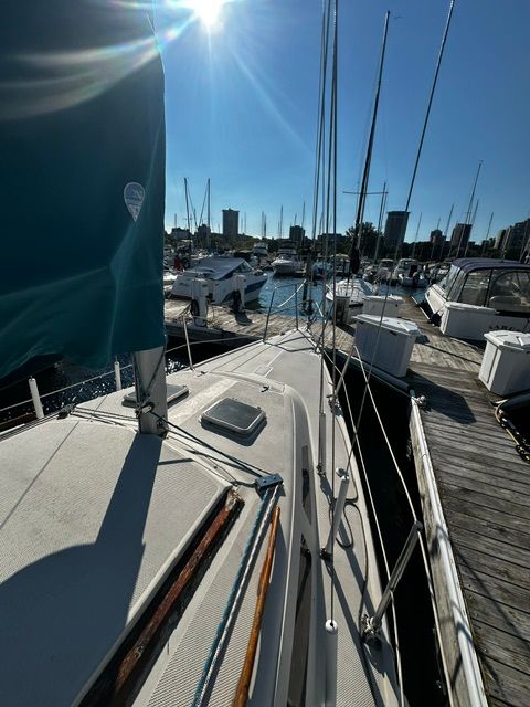 A 1985 Catalina 27 sailboat docked in a marina, surrounded by other boats and buildings.