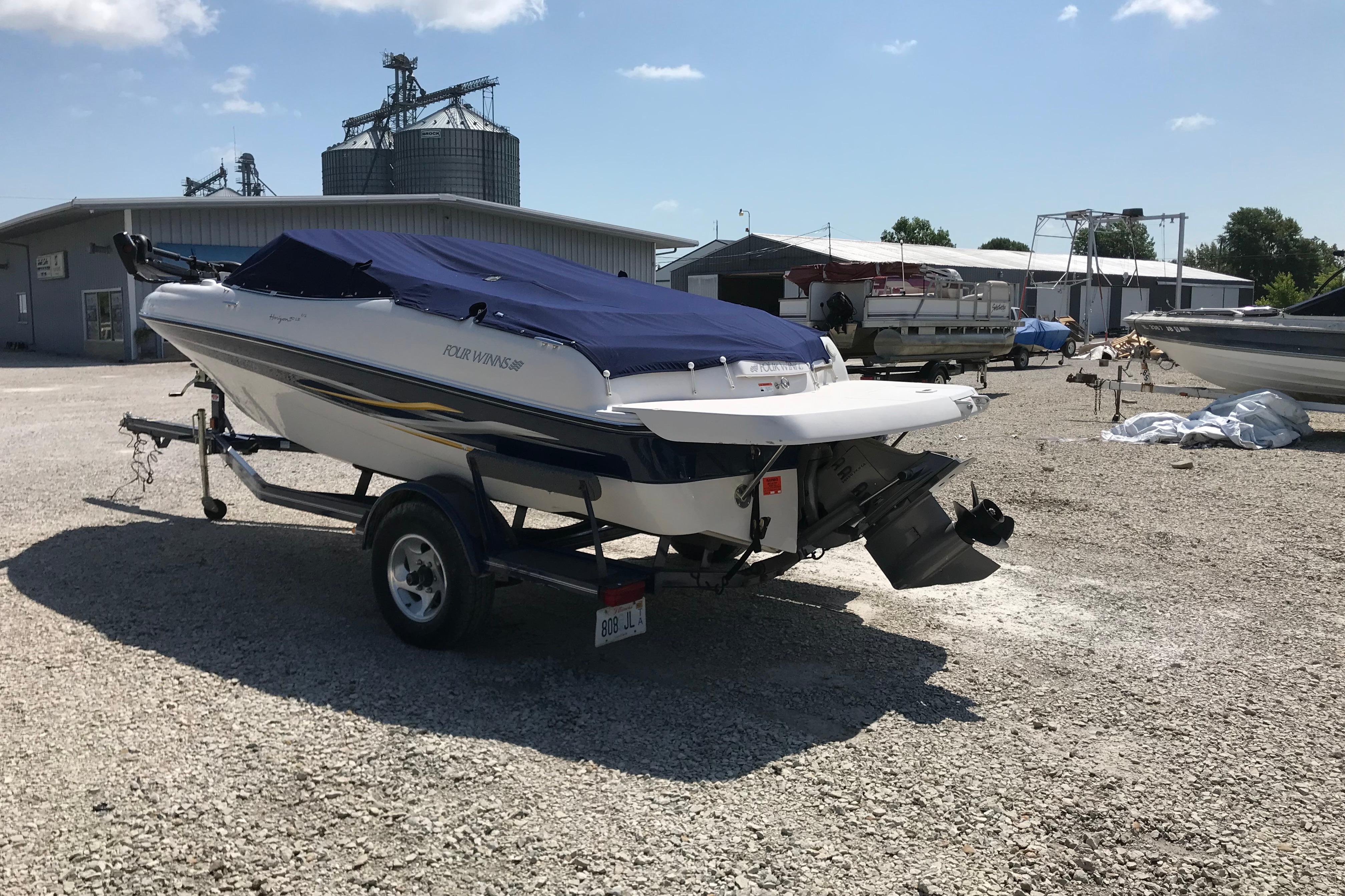 2005 Four Winns 180 Horizon FS boat on trailer, covered, in a gravel lot.