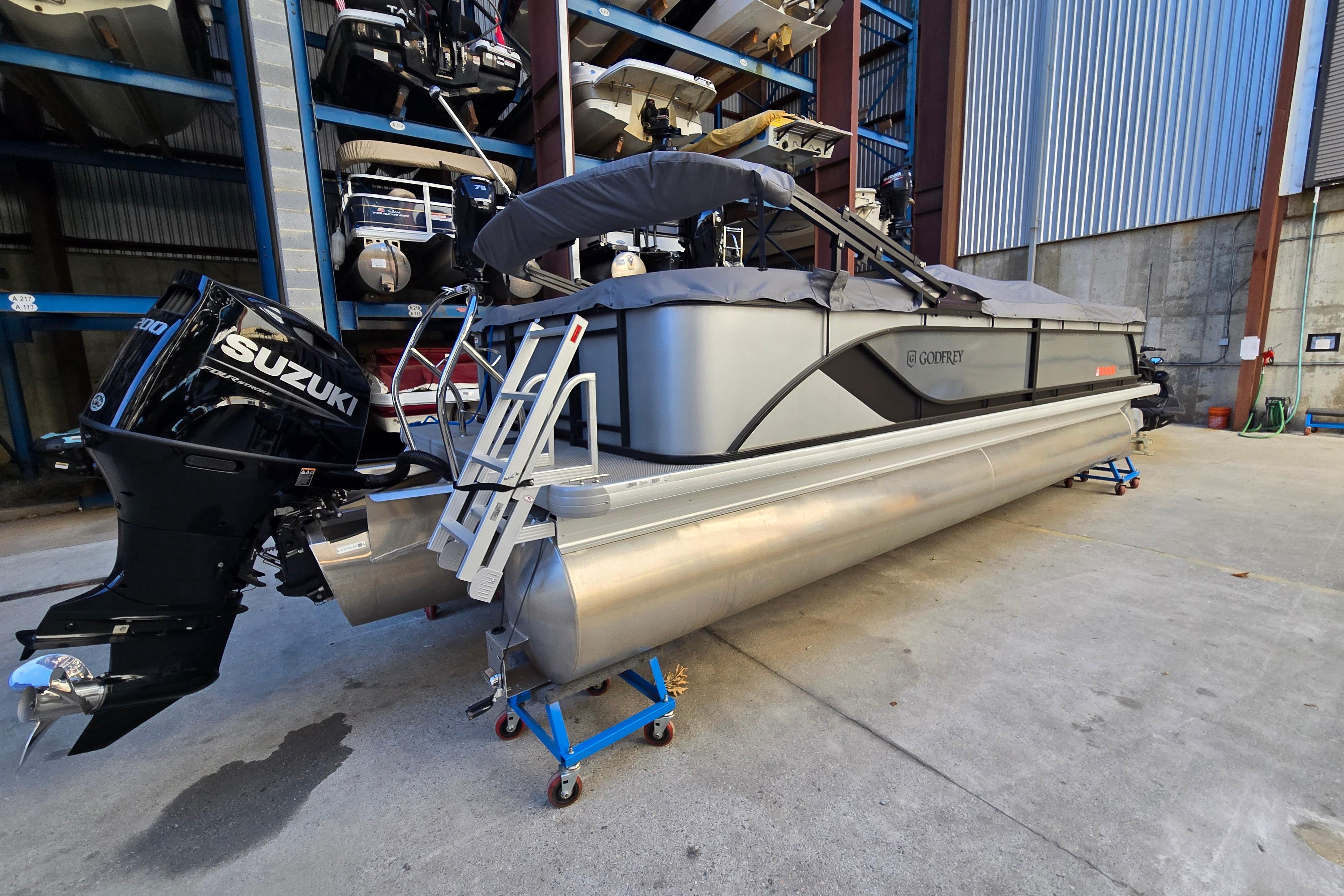 2024 Godfrey Sweetwater 2486 SB pontoon boat with Suzuki outboard motor in storage facility.