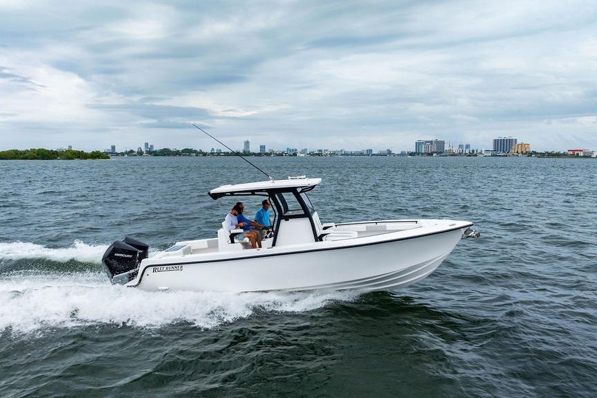 2027 Reef Runner 280 boat cruising on open water with city skyline in background.