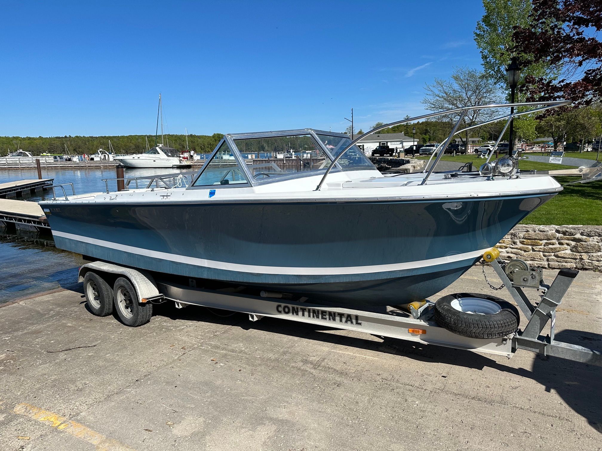 A 1969 John Allmand Citation II boat on a trailer by the shore.