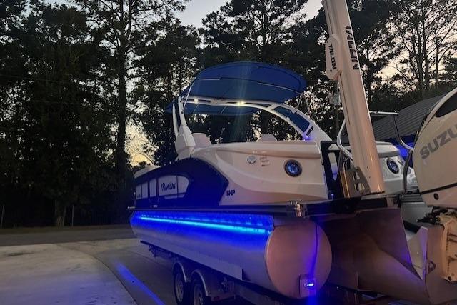 2020 Manitou 25 X-Plode RFW pontoon boat with blue LED lights, parked outdoors.