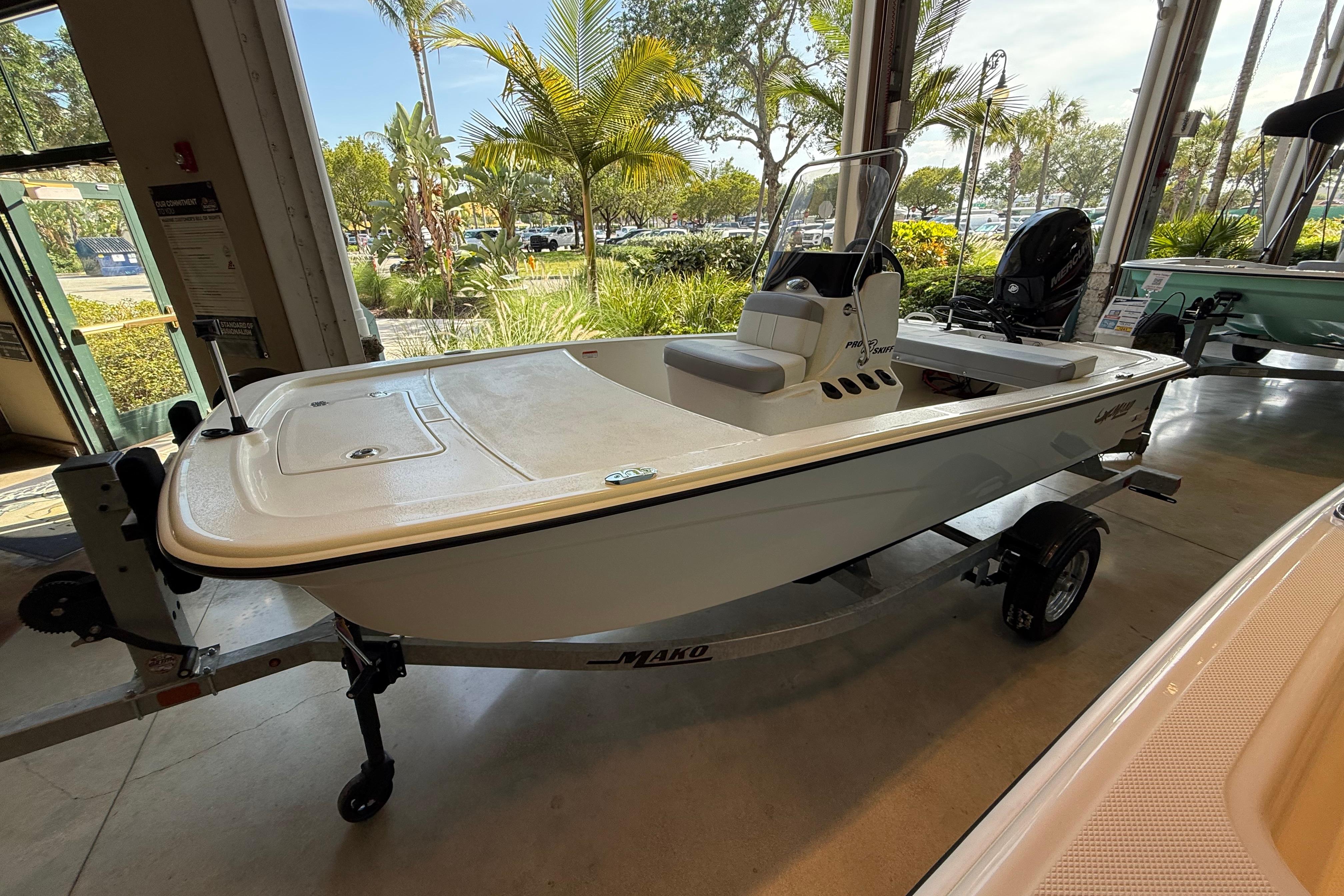 2026 Mako Pro Skiff 13 CC boat displayed indoors with lush greenery outside.