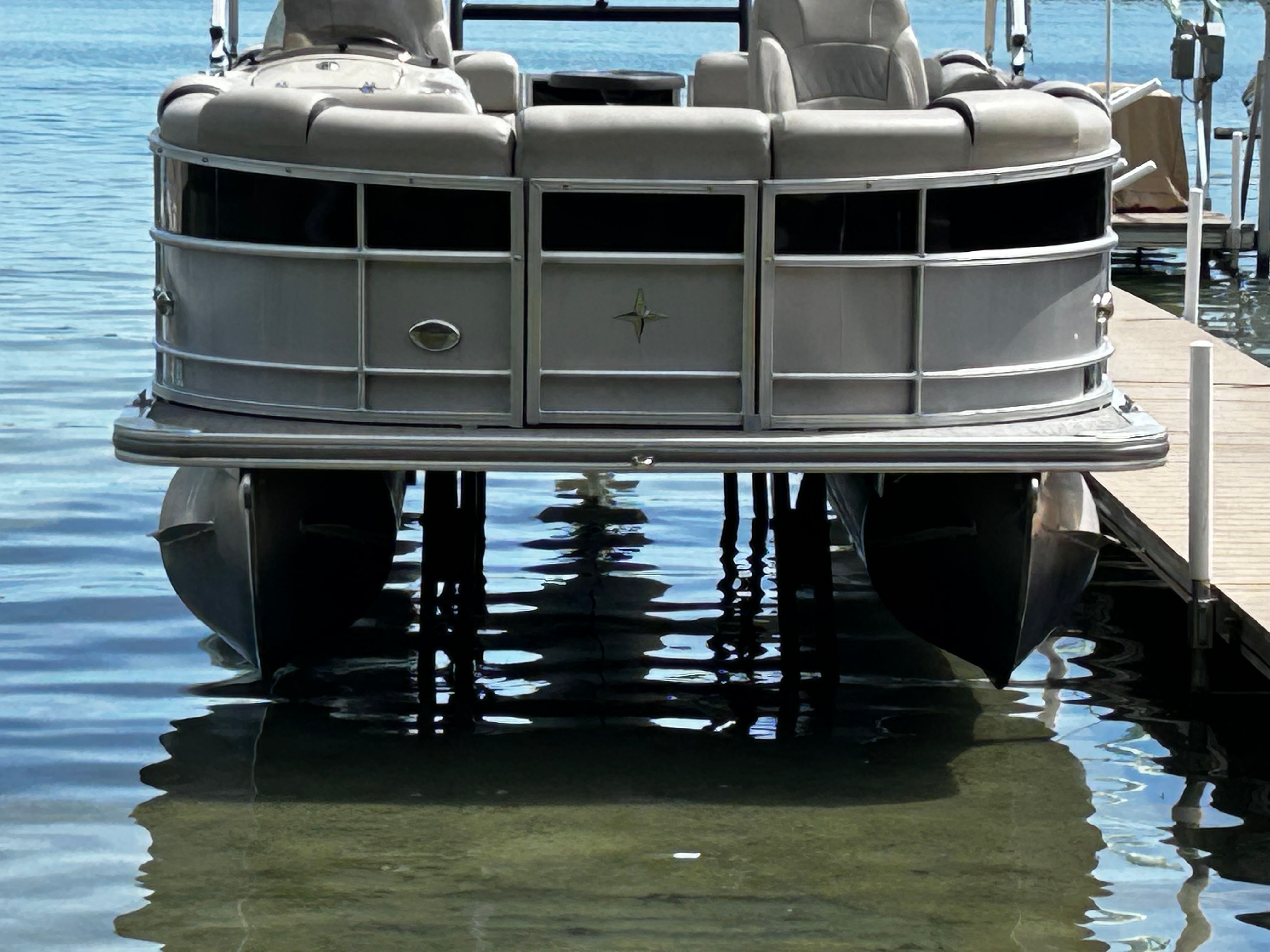 A pontoon boat is docked at a pier, with clear water beneath.