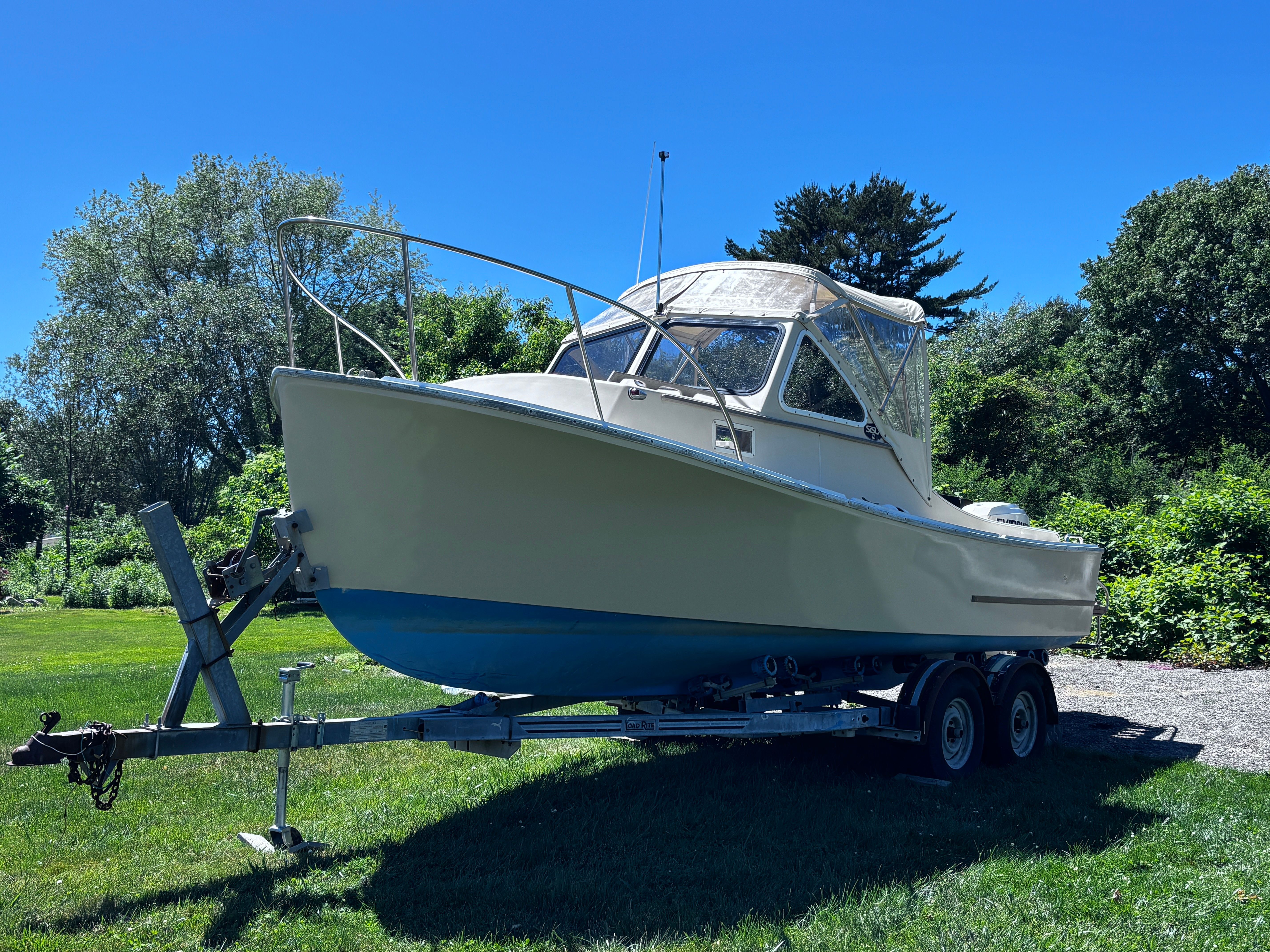 A 1984 SISU 22’ Bass boat on a trailer, surrounded by green landscape.