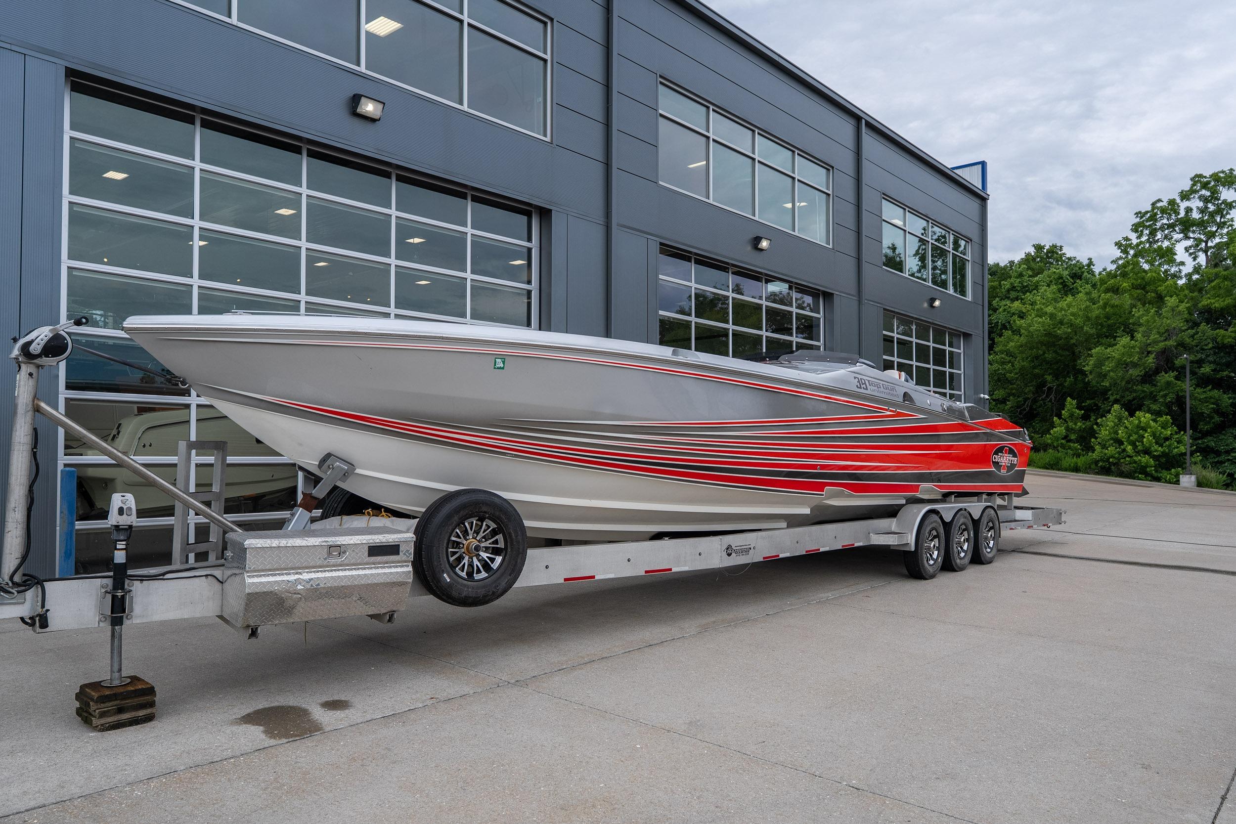2006 Cigarette 39' Top Gun Unlimited boat on trailer outside modern building.