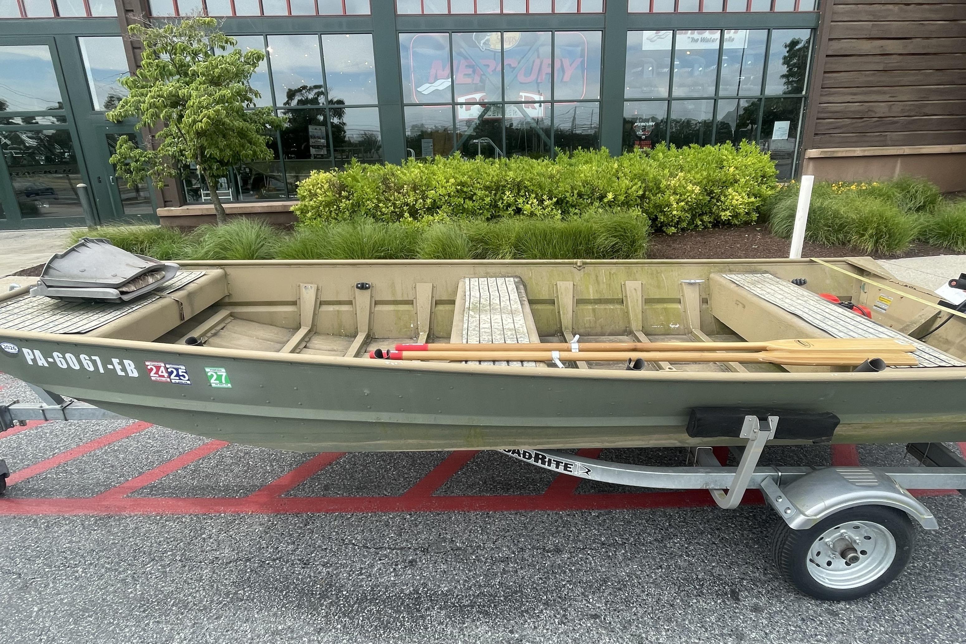 1986 Landau 1664 Jon boat on trailer, parked outside a building with greenery.
