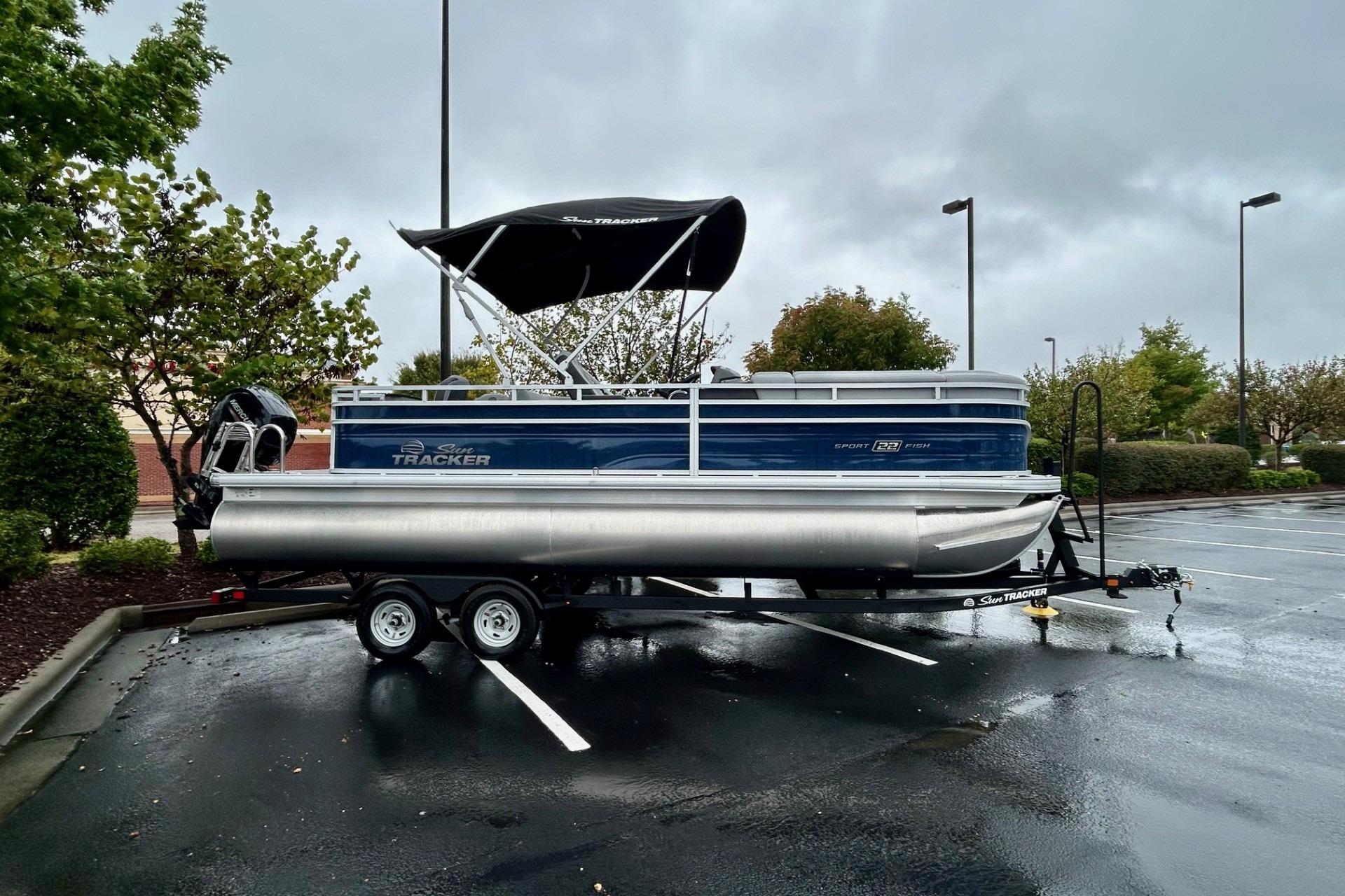 2026 Sun Tracker SportFish 22 DLX pontoon boat on trailer in parking lot.