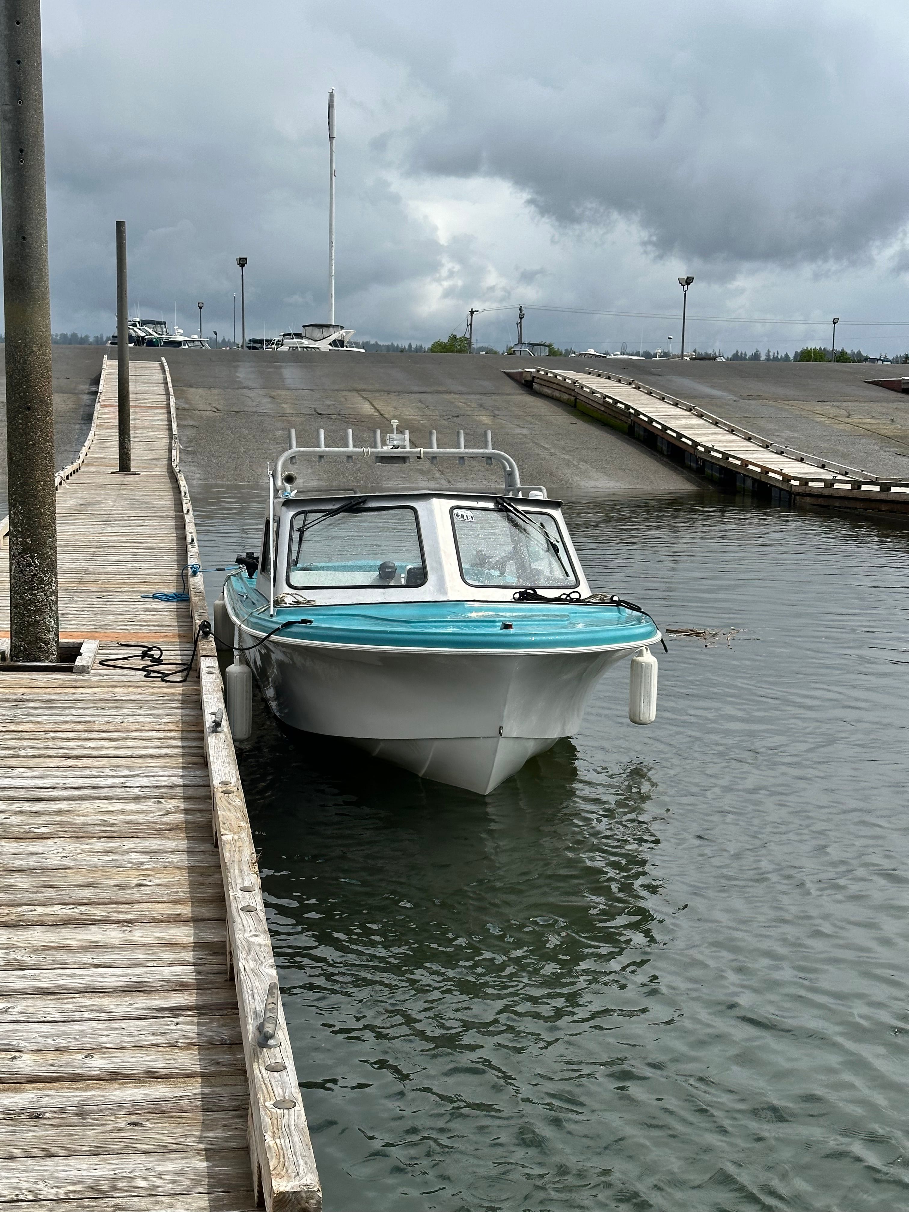 A restored 1967 Fiberform boat is docked at a wooden pier in a calm harbor.