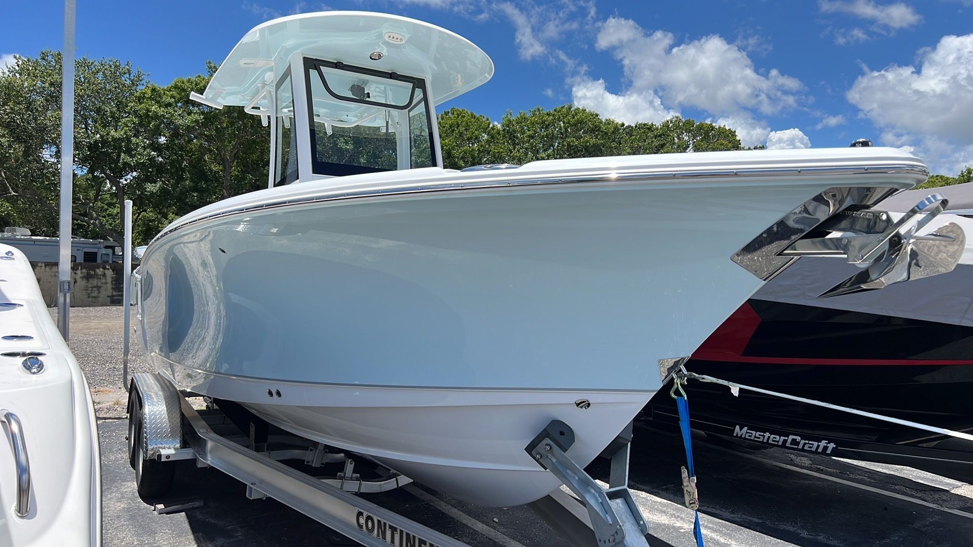 A 2024 Sea Hunt Ultra 265 SE boat on a trailer, surrounded by trees and a blue sky.
