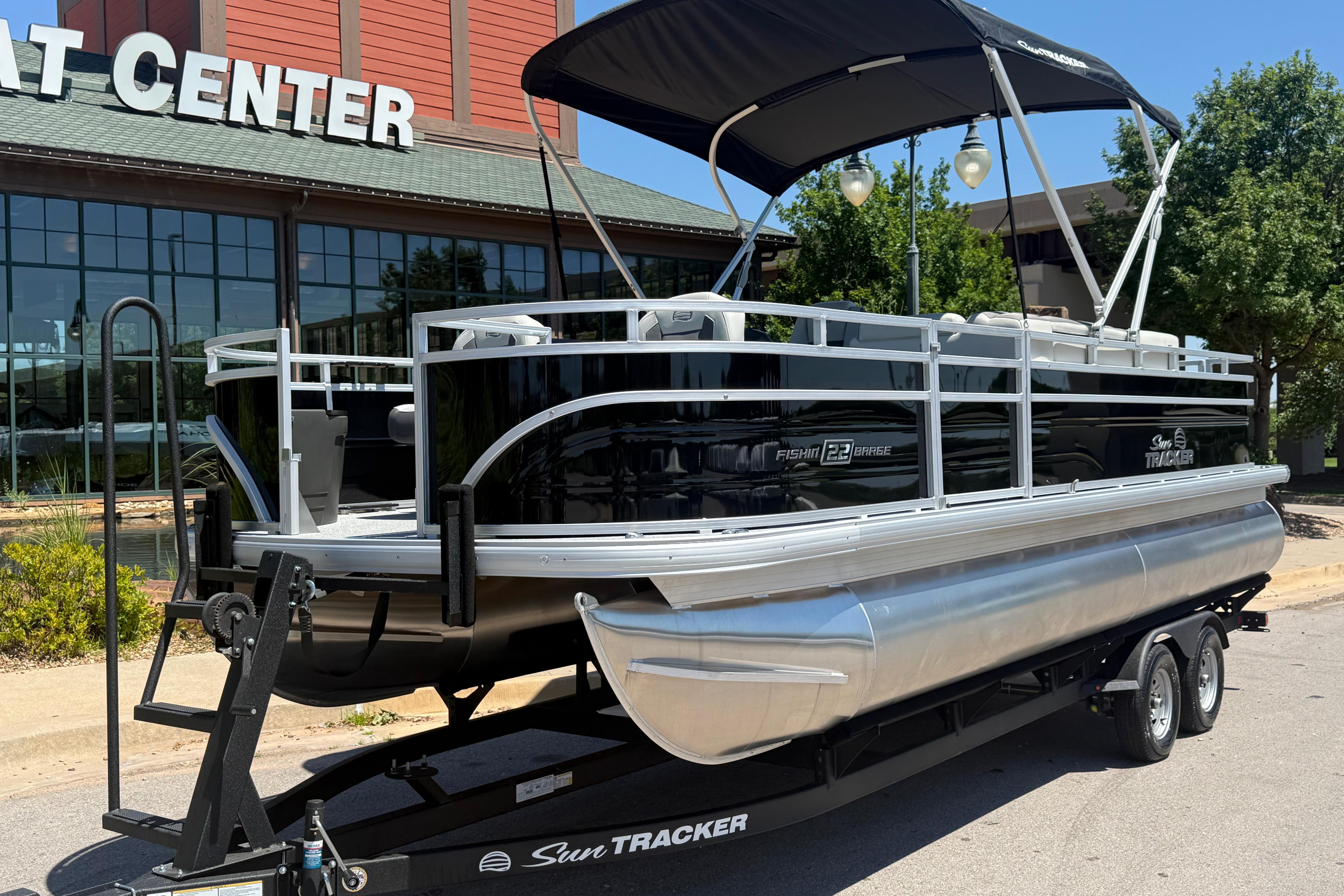 2026 Sun Tracker Fishin' Barge 22 DLX pontoon boat on trailer outside dealership.