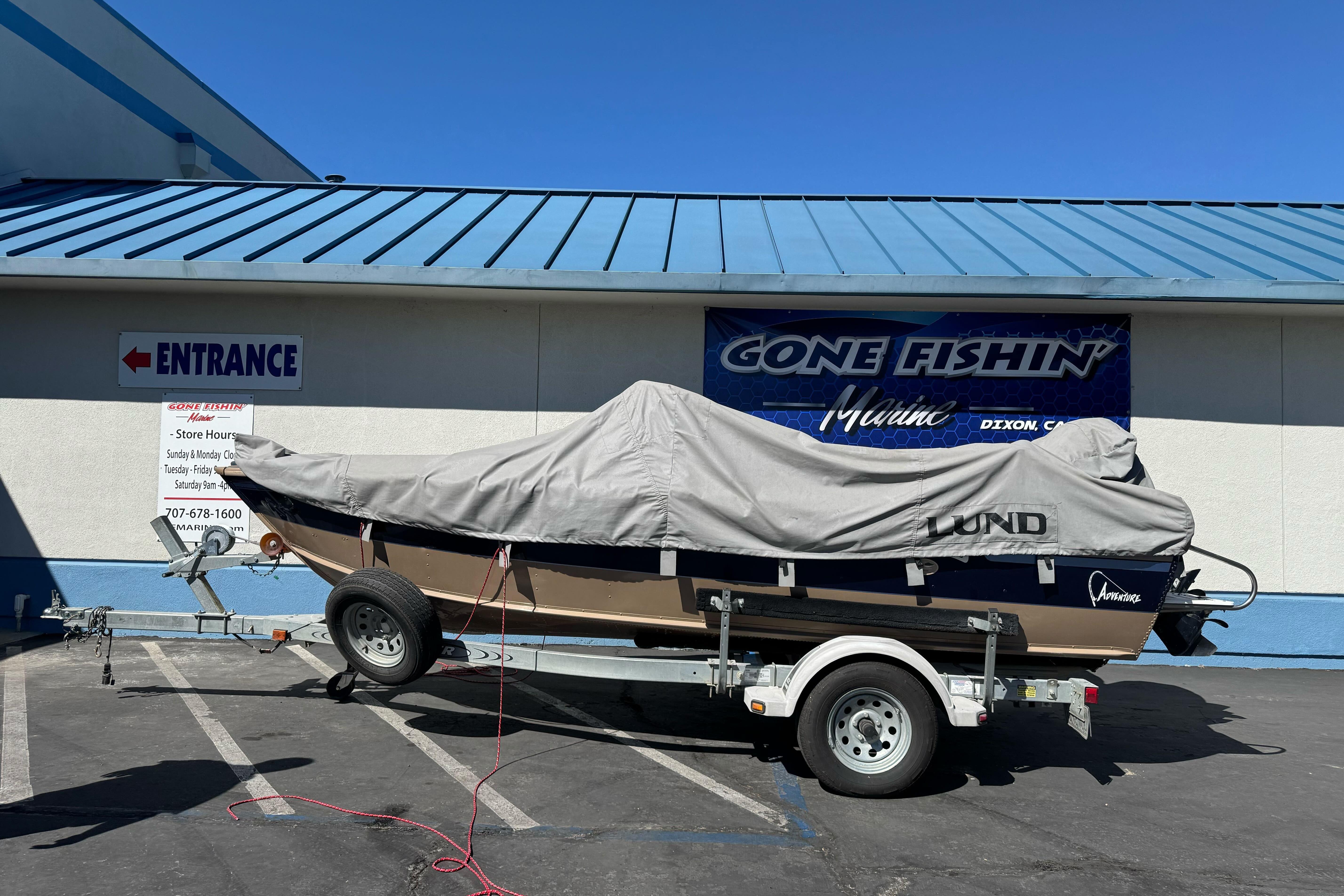 1998 Lund 1700 Pro Sport boat covered on trailer outside marine store.