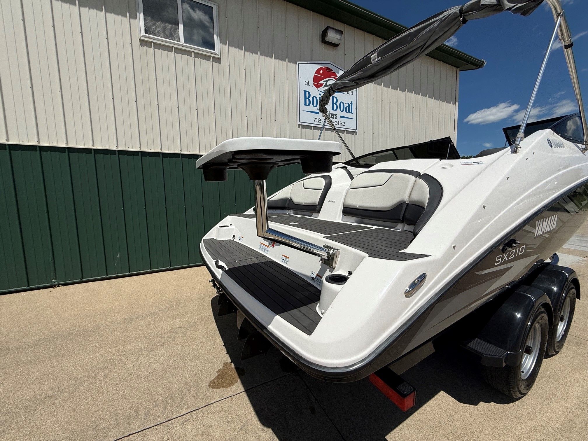 Yamaha SX210 boat on a trailer in front of a building with a sign.