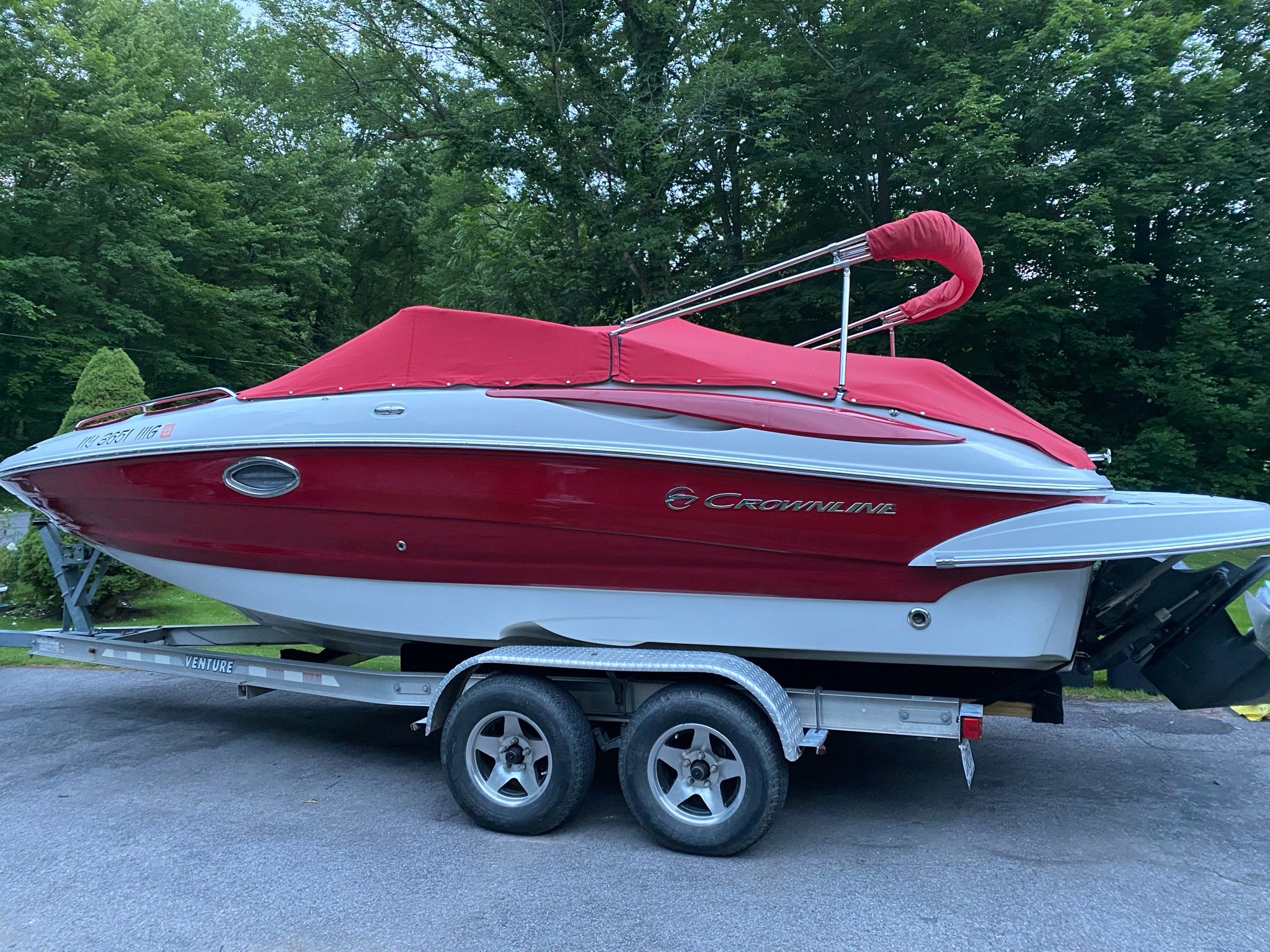2009 Crownline 220 EX with a red cover on a trailer, surrounded by trees.