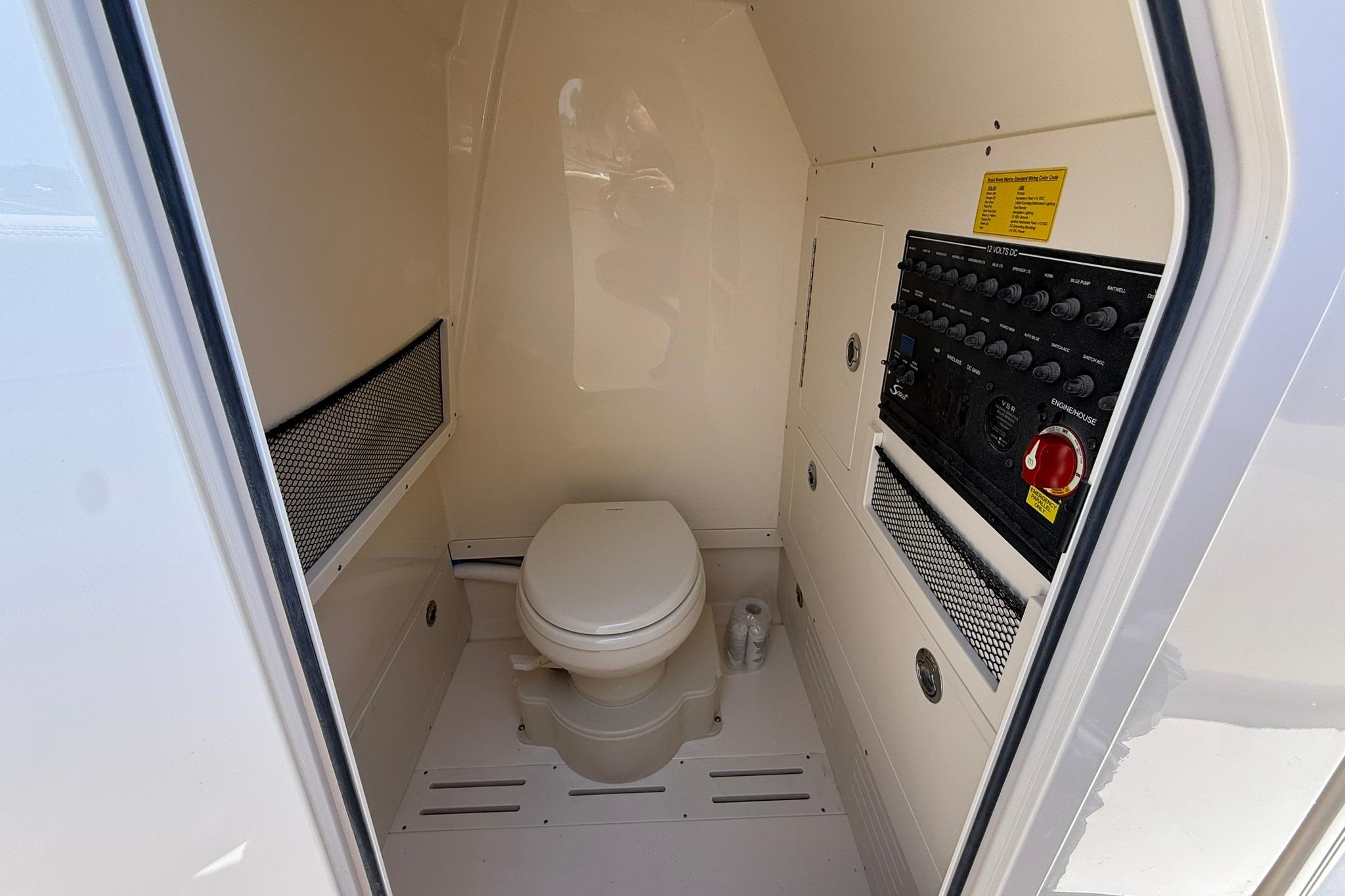 Interior of a 2027 Scout 240 XSF boat featuring a compact marine toilet and control panel.