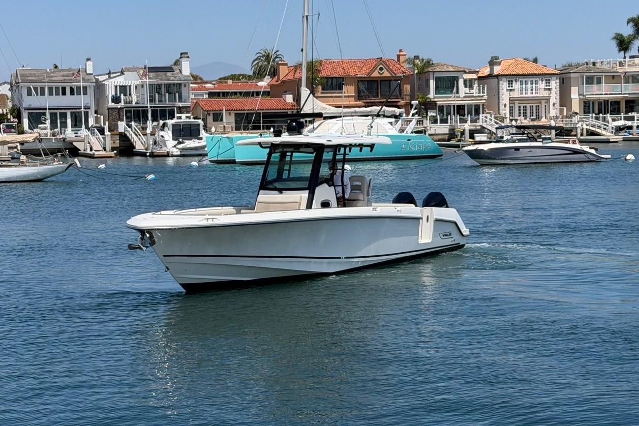 2021 Boston Whaler 330 Outrage cruising in a scenic harbor with waterfront homes.