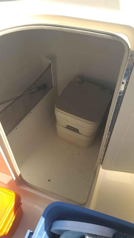 A storage compartment in the boat with a portable toilet and mesh pocket.