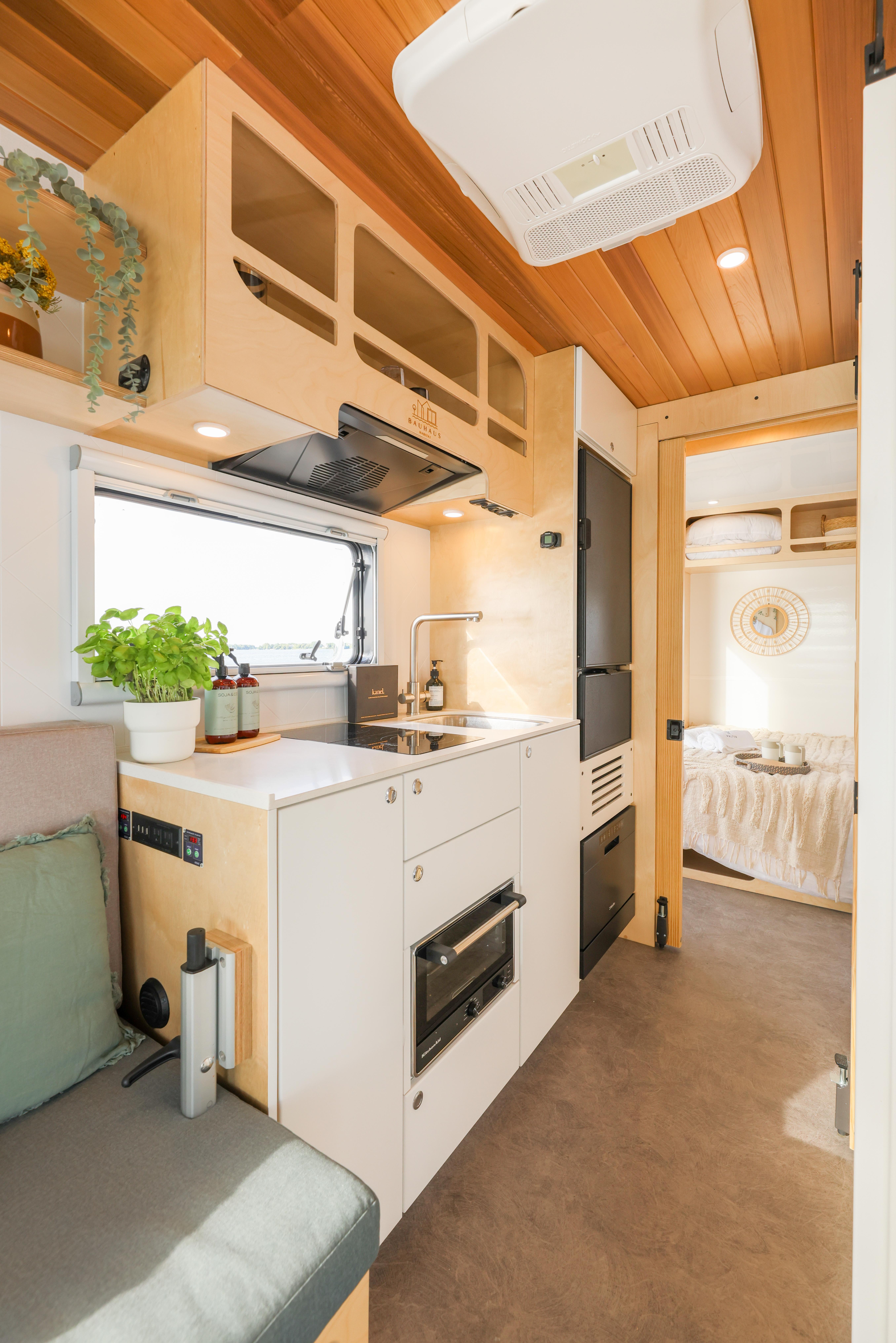 Modern camper interior with kitchenette, wooden ceiling, and cozy sleeping area in a 2023 Custom Walter 450.