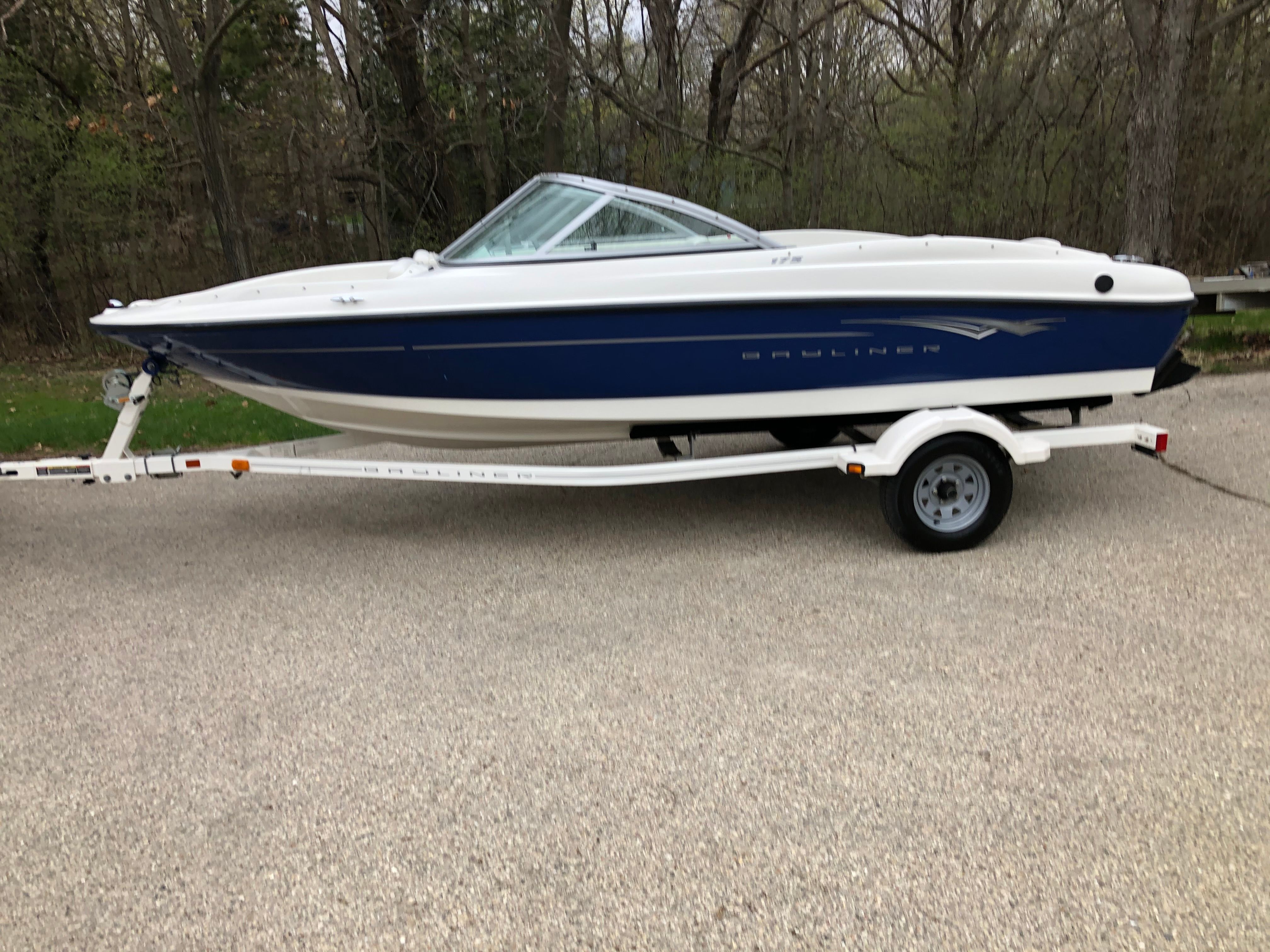 A Bayliner 175 Bowrider boat on a trailer, surrounded by trees.